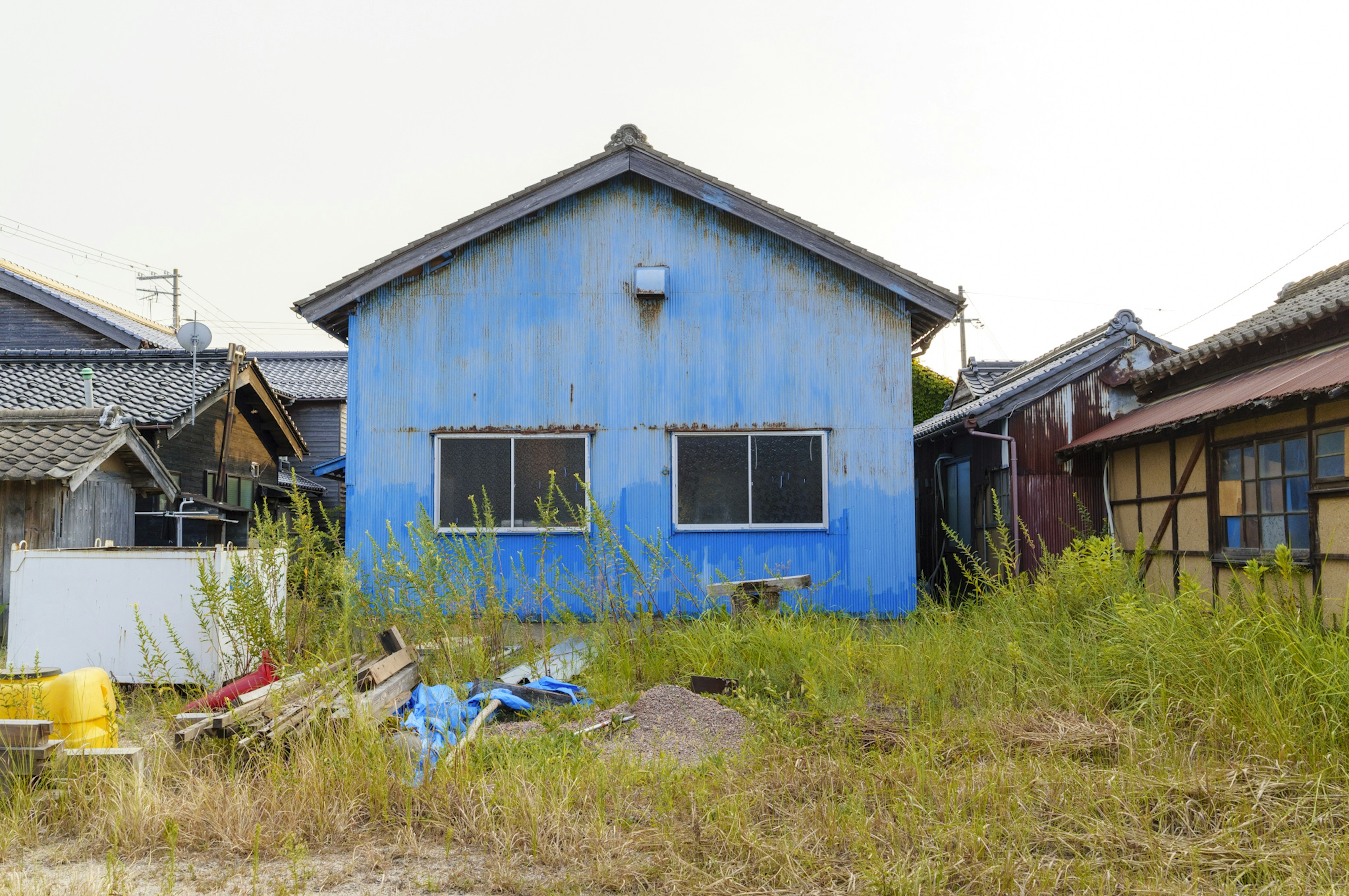 Rumah tua dengan eksterior biru dikelilingi oleh rumput tinggi