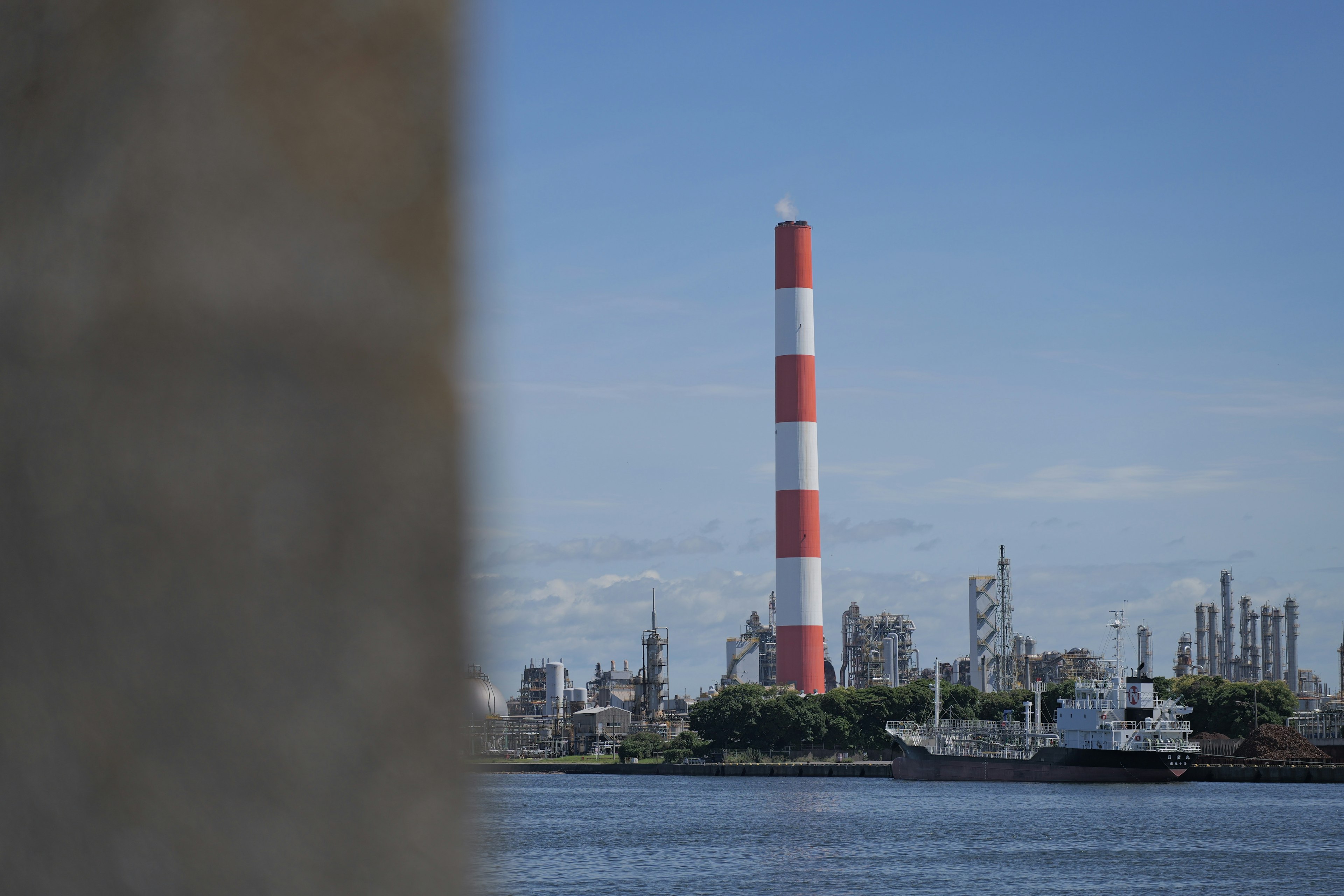 Chimenea roja y blanca con área industrial al fondo