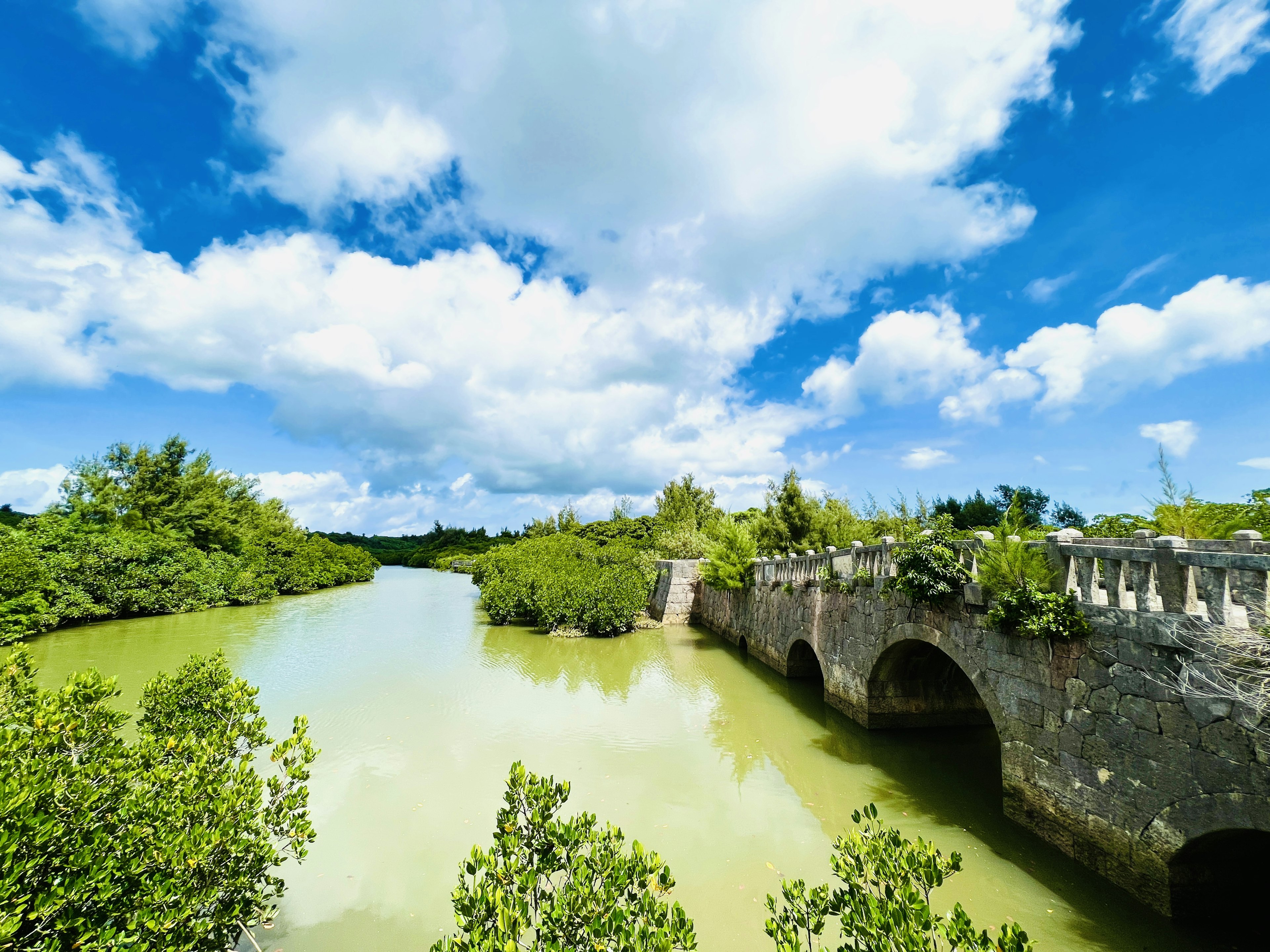 Una vista escénica que muestra un río de agua verde y un viejo puente de piedra bajo un cielo azul con nubes blancas