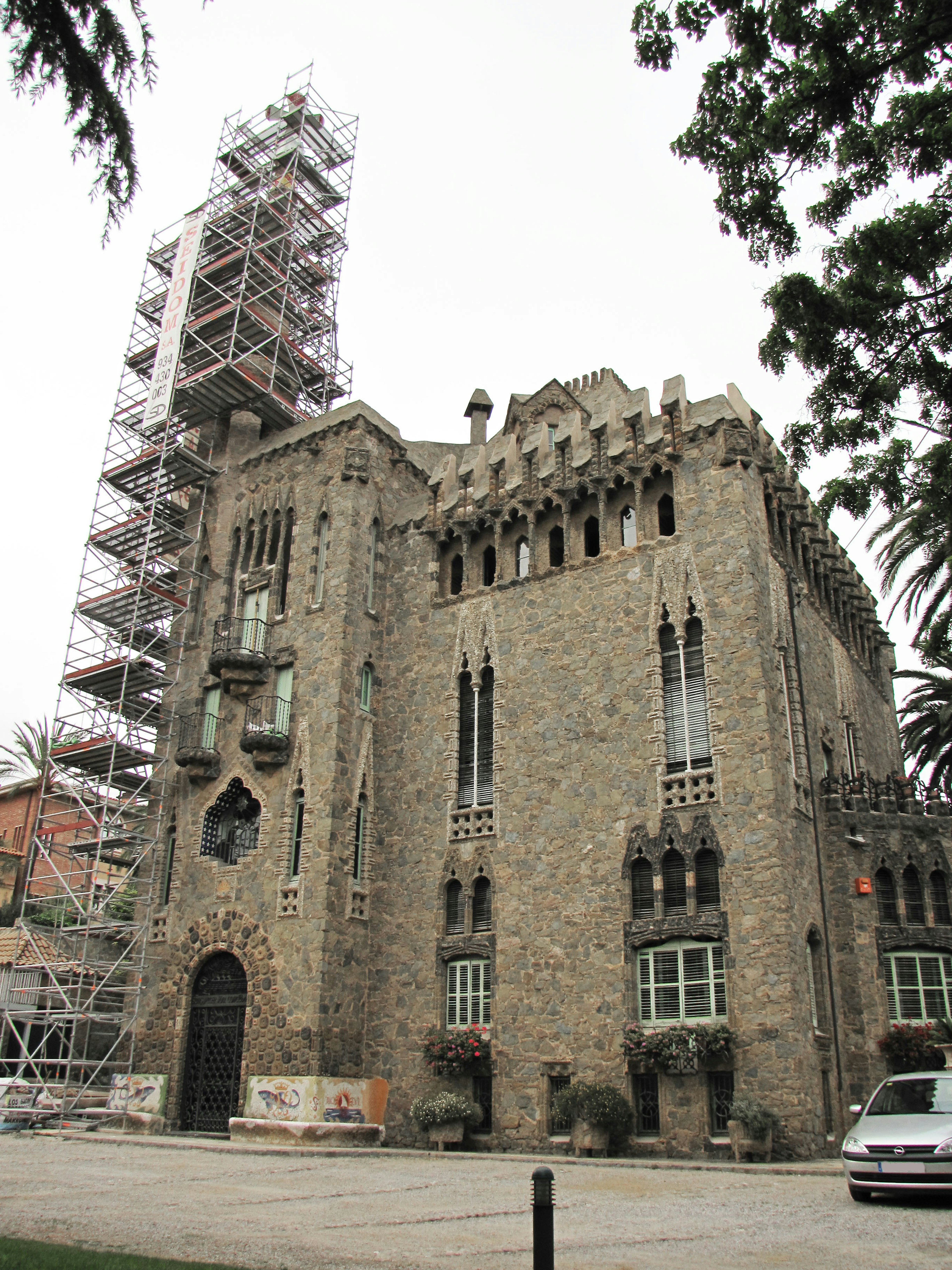 Stone castle-like building under renovation surrounded by green trees with scaffolding on the left