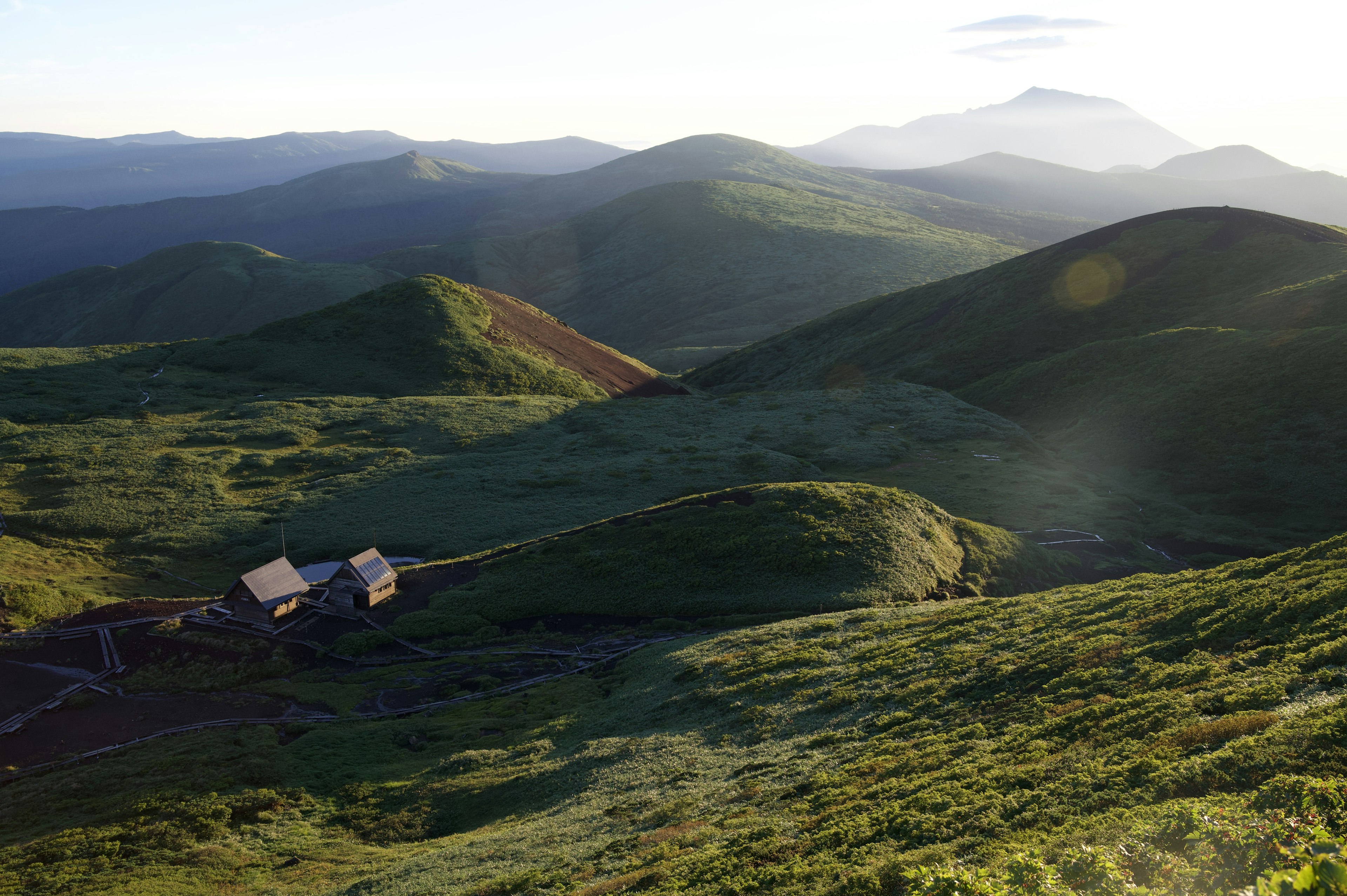 緑の丘陵と小屋の風景で、遠くに山が見える