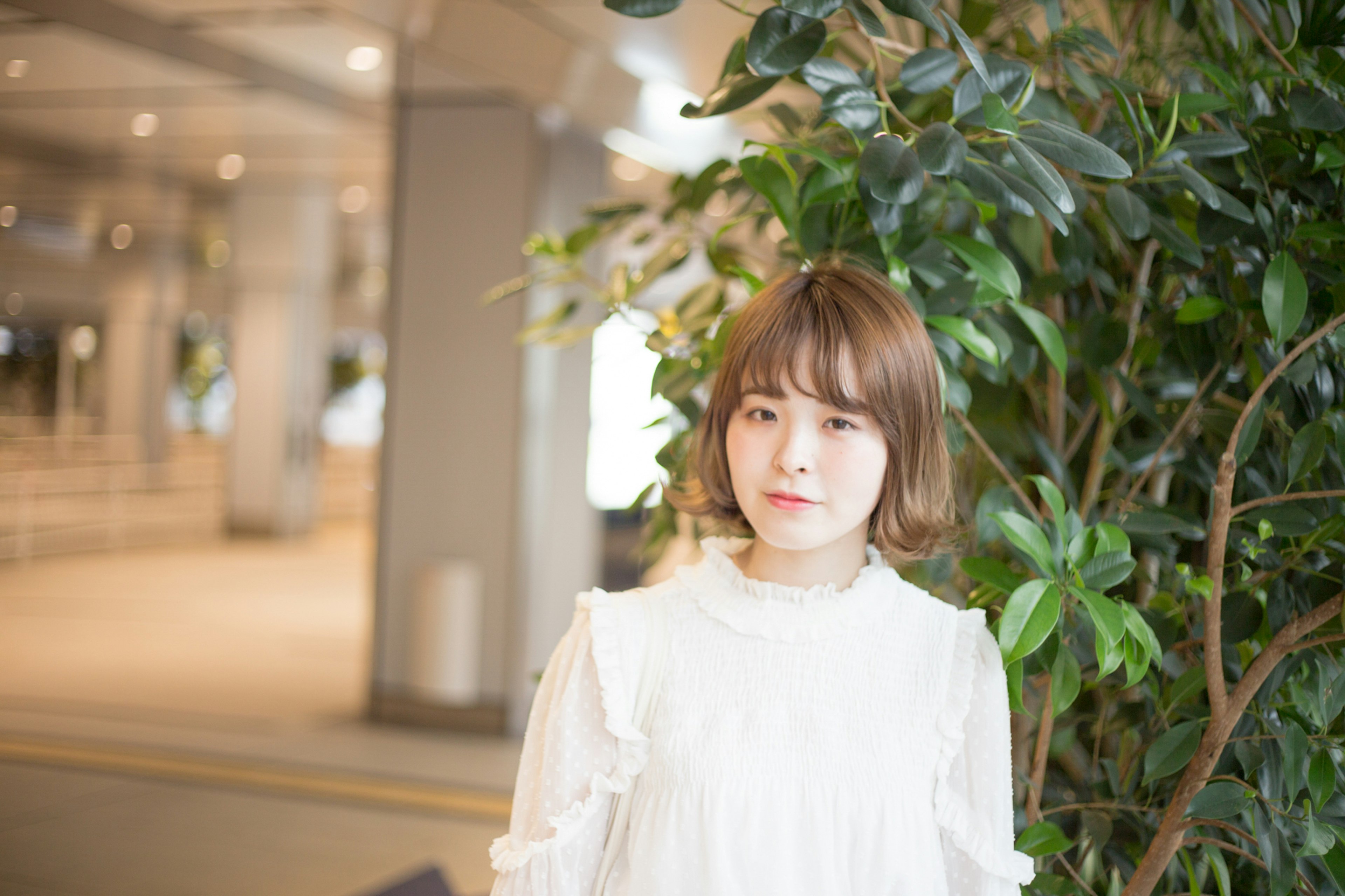 A woman in a white blouse smiling in front of plants