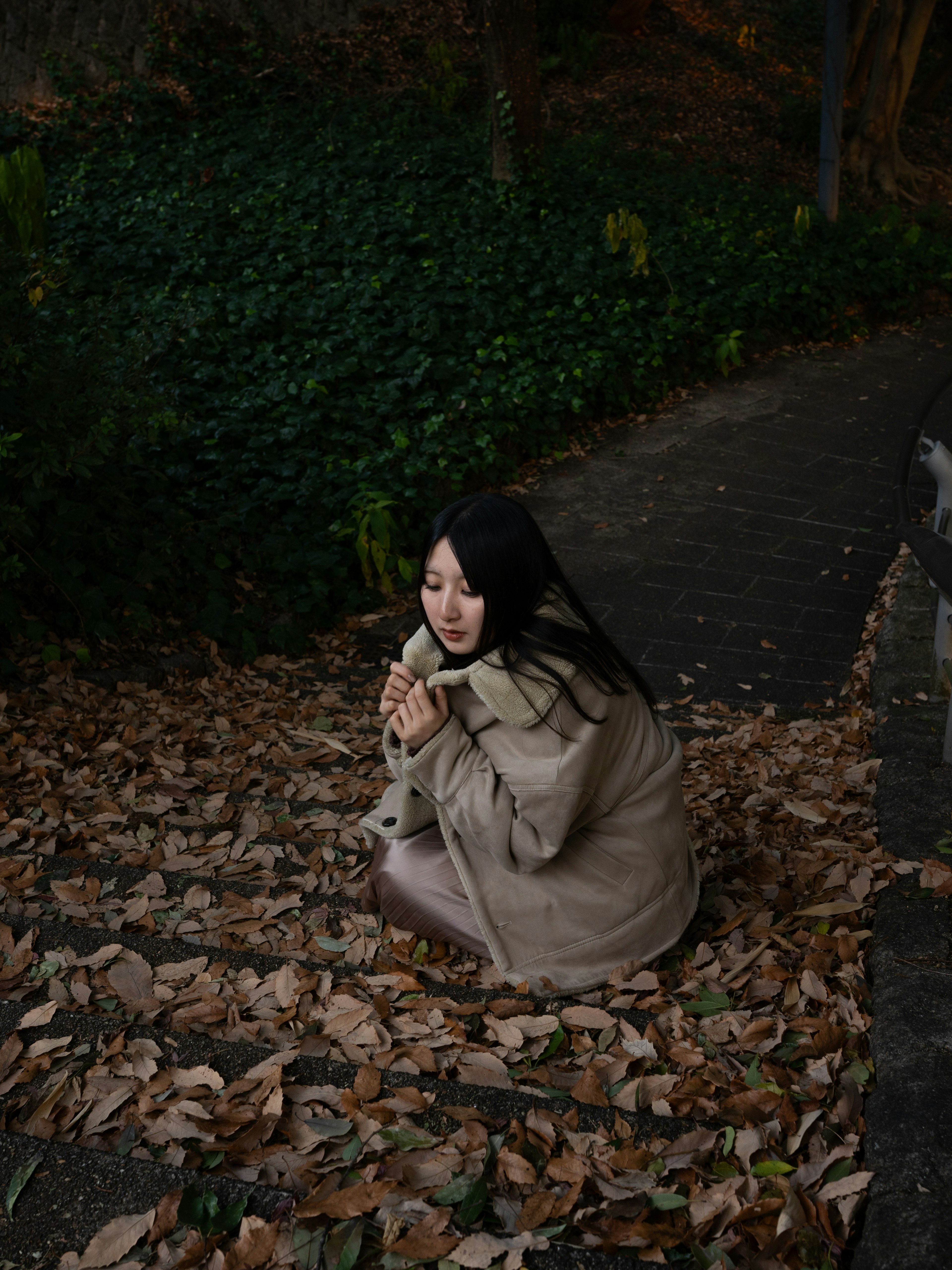 A woman sitting on fallen leaves surrounded by green plants