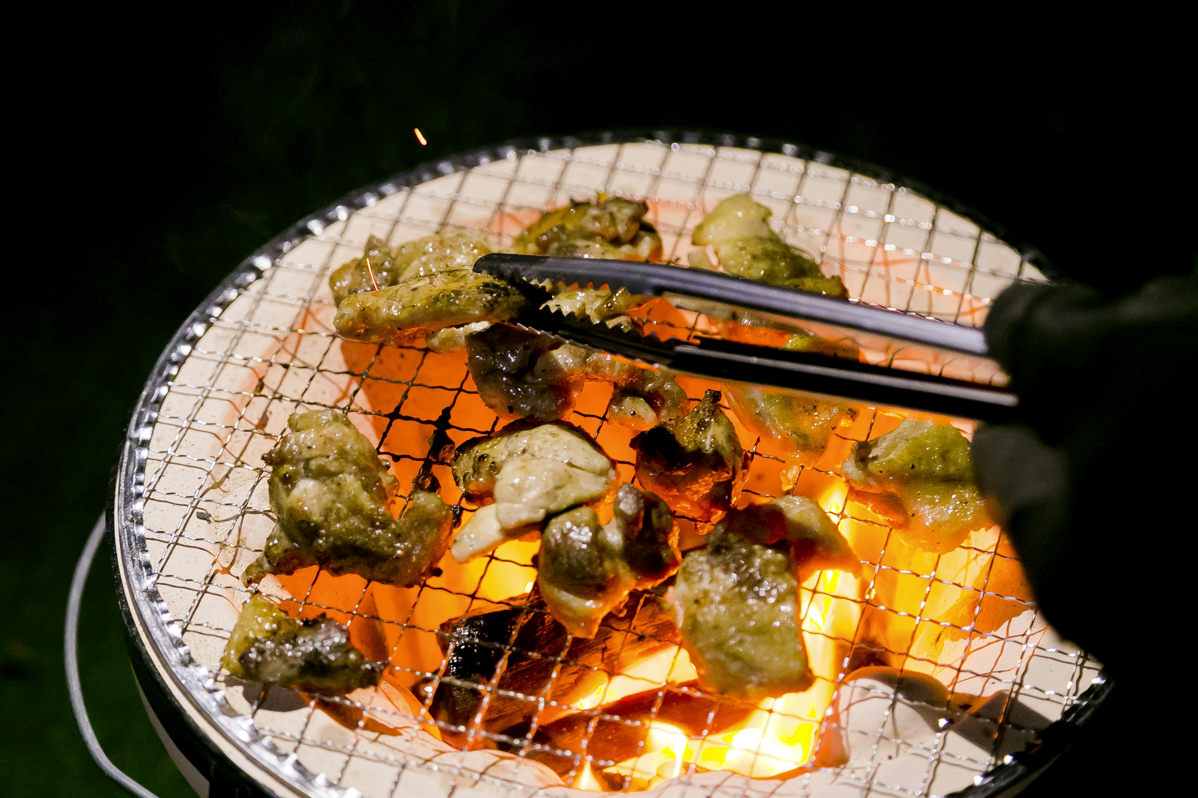 Grilled meat pieces being handled with tongs over glowing charcoal