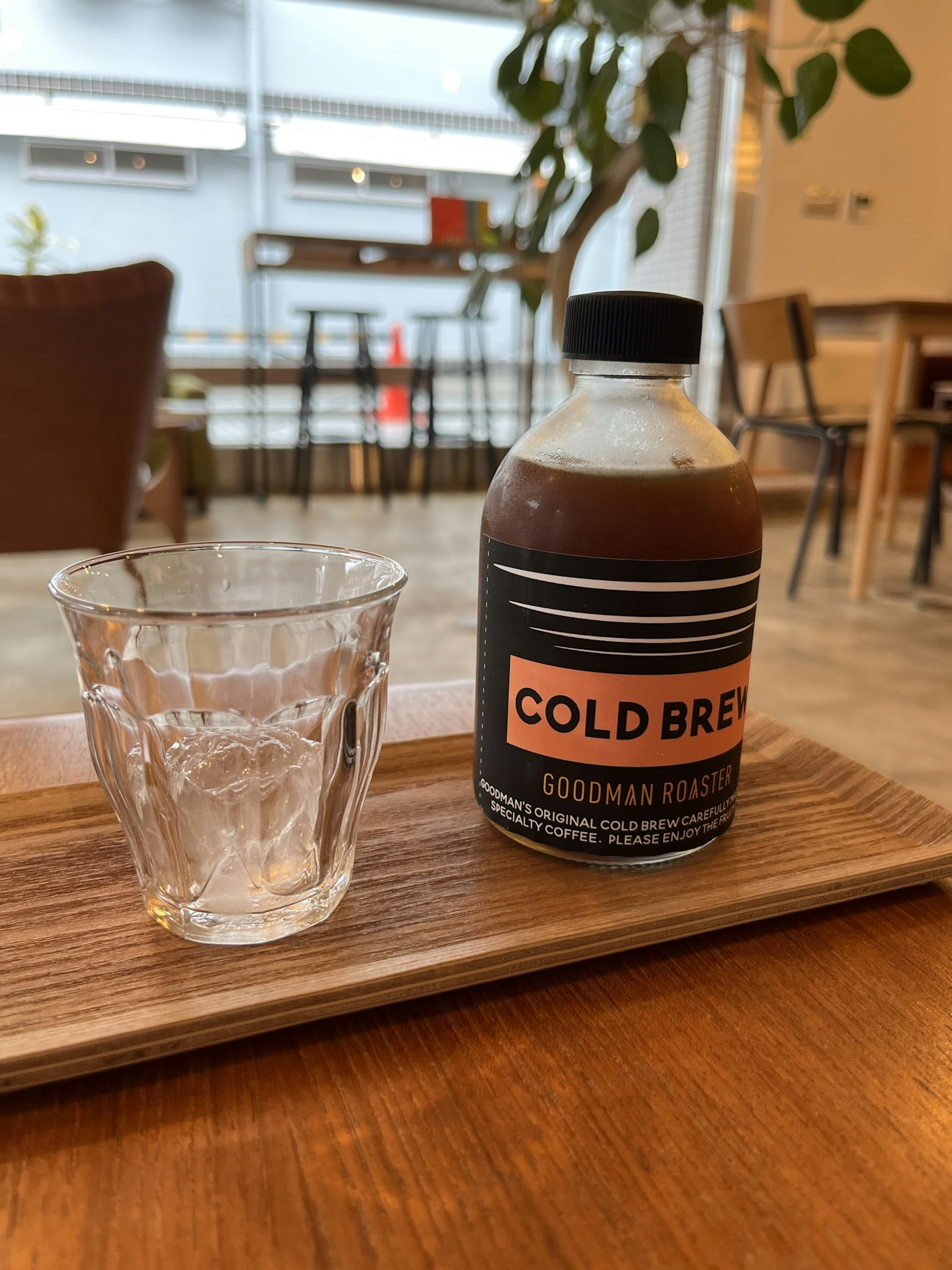 Una bottiglia di caffè cold brew e un bicchiere su un vassoio di legno in un caffè