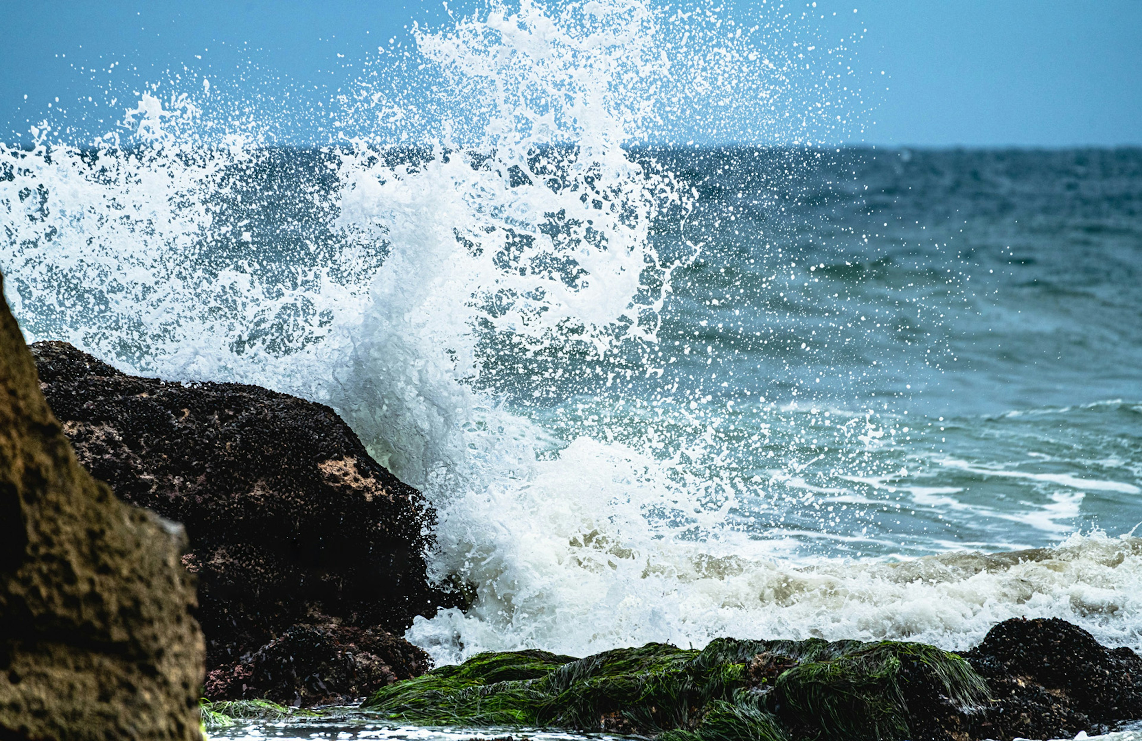 Olas rompiendo contra la costa rocosa con salpicaduras y cielo azul