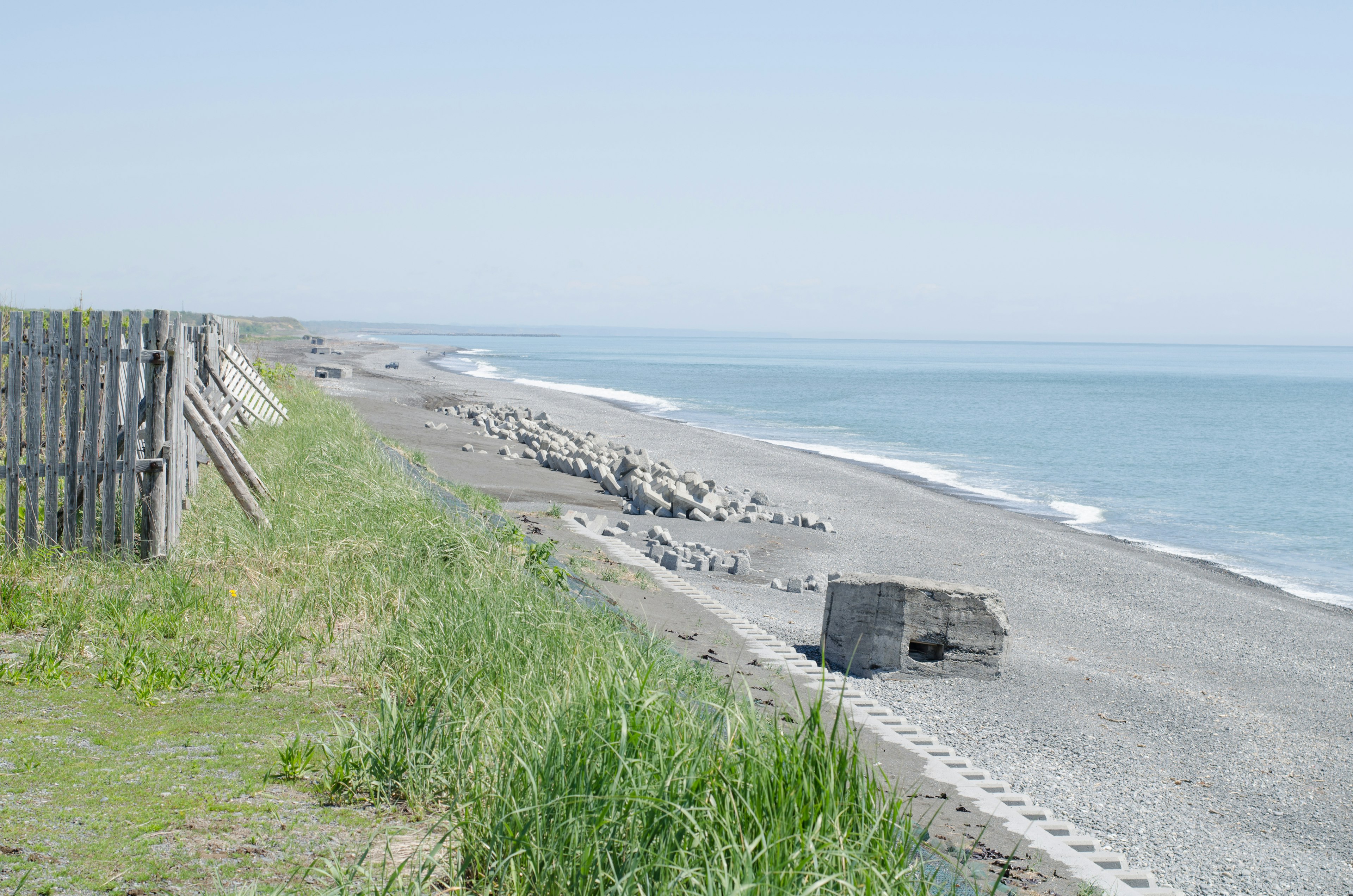 Ruhige Strandlandschaft mit sichtbarem Küstenbereich Gras und verstreute Steine am Kiesstrand