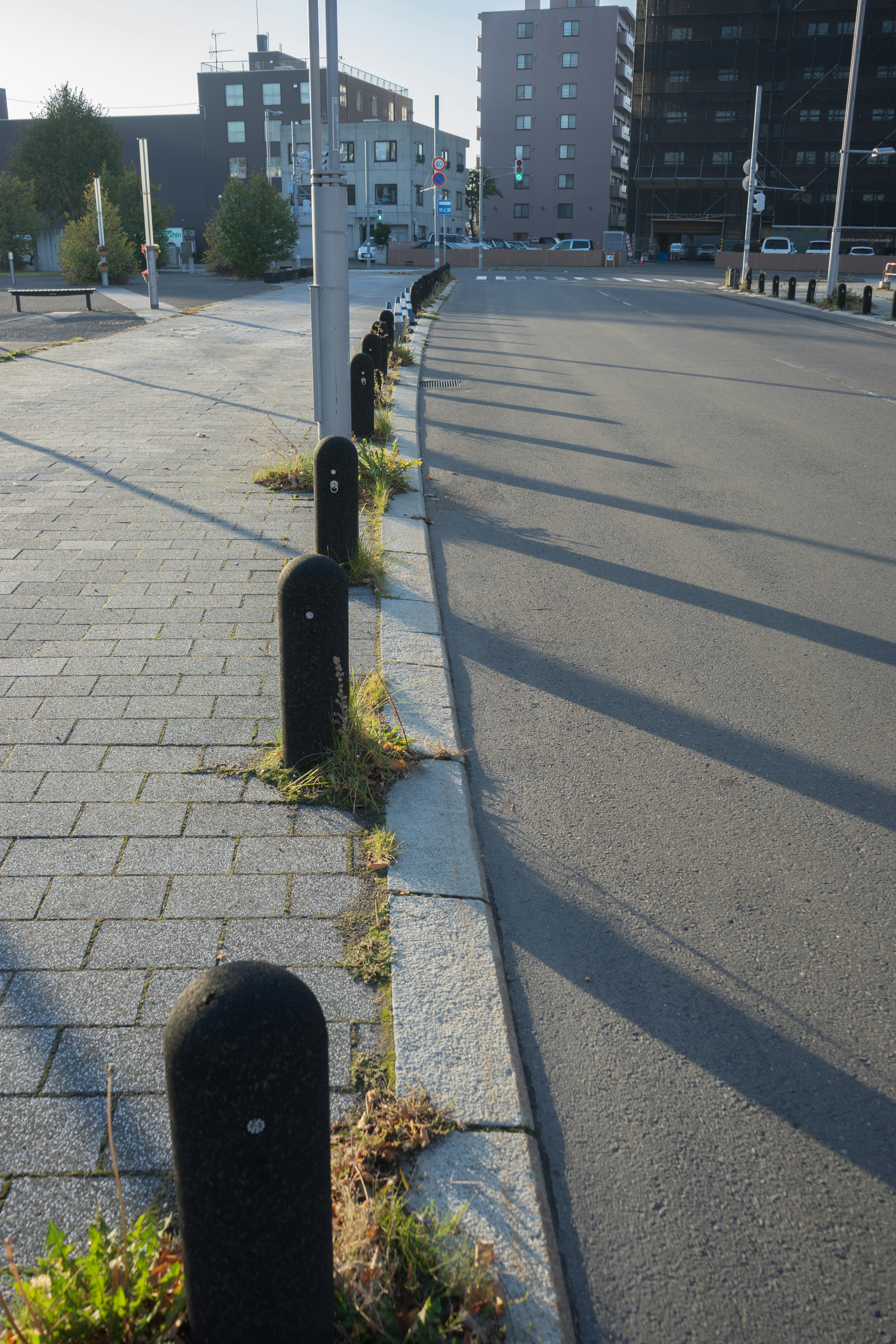 Bollard hitam di sepanjang jalan berbatu dengan bayangan panjang