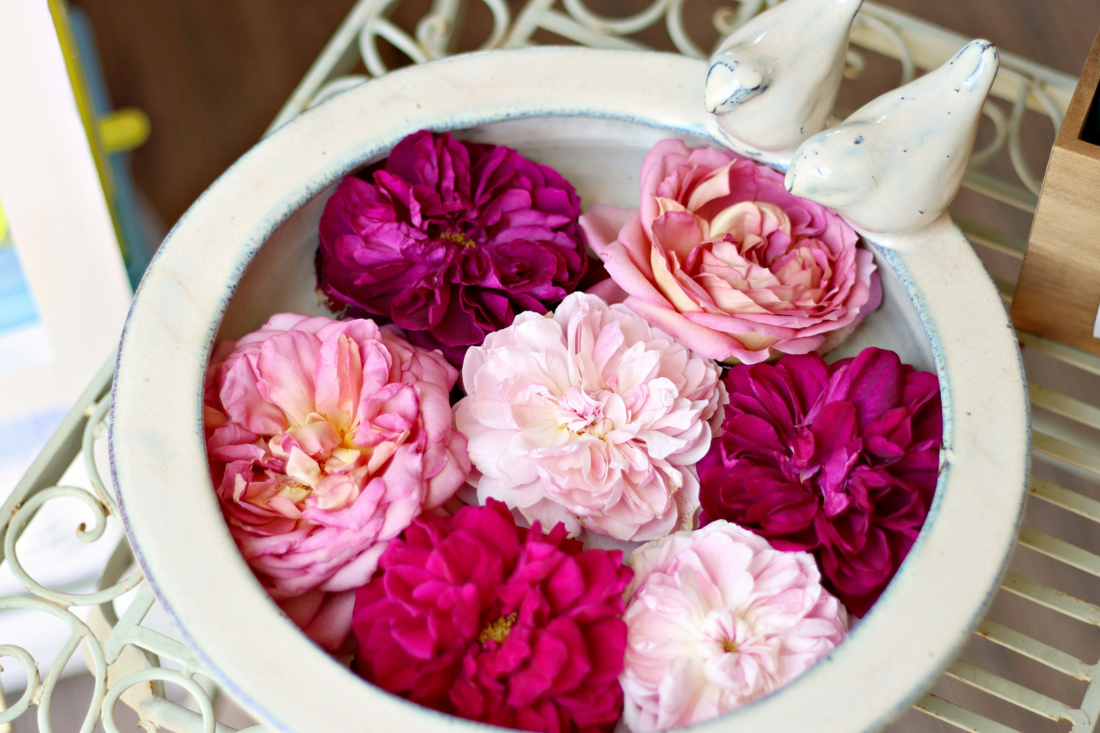 A white bowl filled with pink and purple flowers and a small white bird figurine