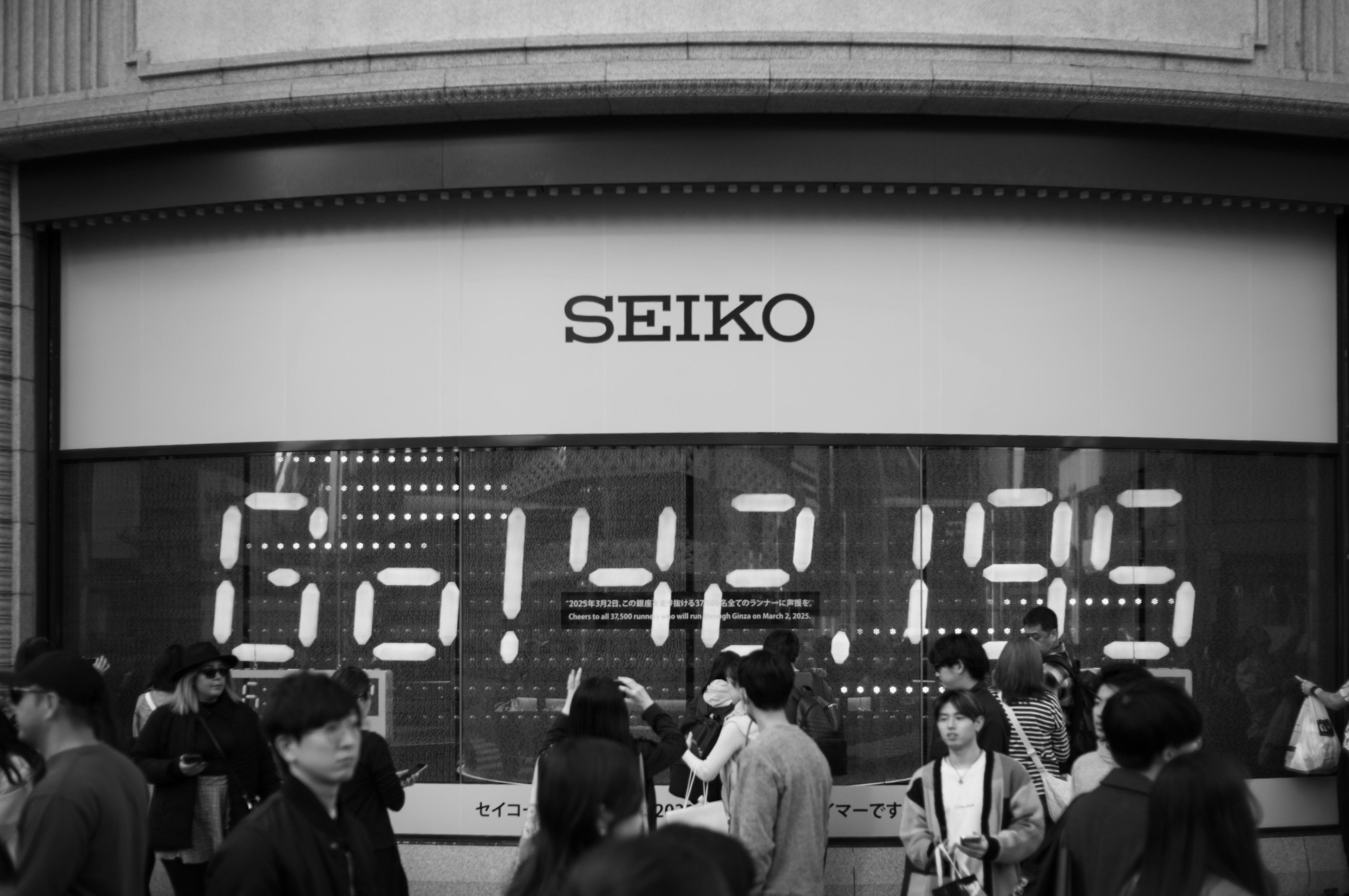 People gathered in front of a Seiko watch store featuring a large digital clock