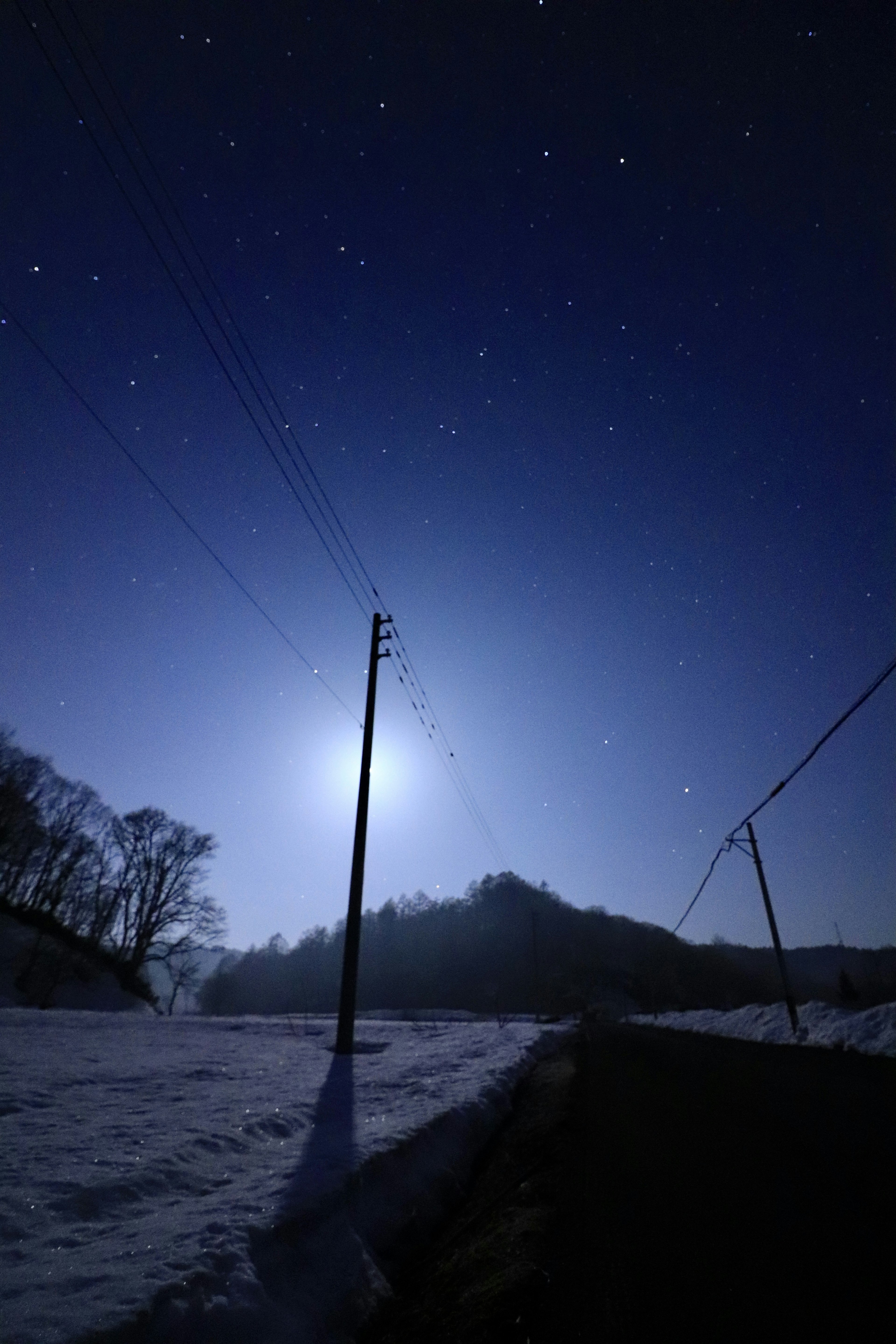 A snowy road with a power pole under a starry night sky