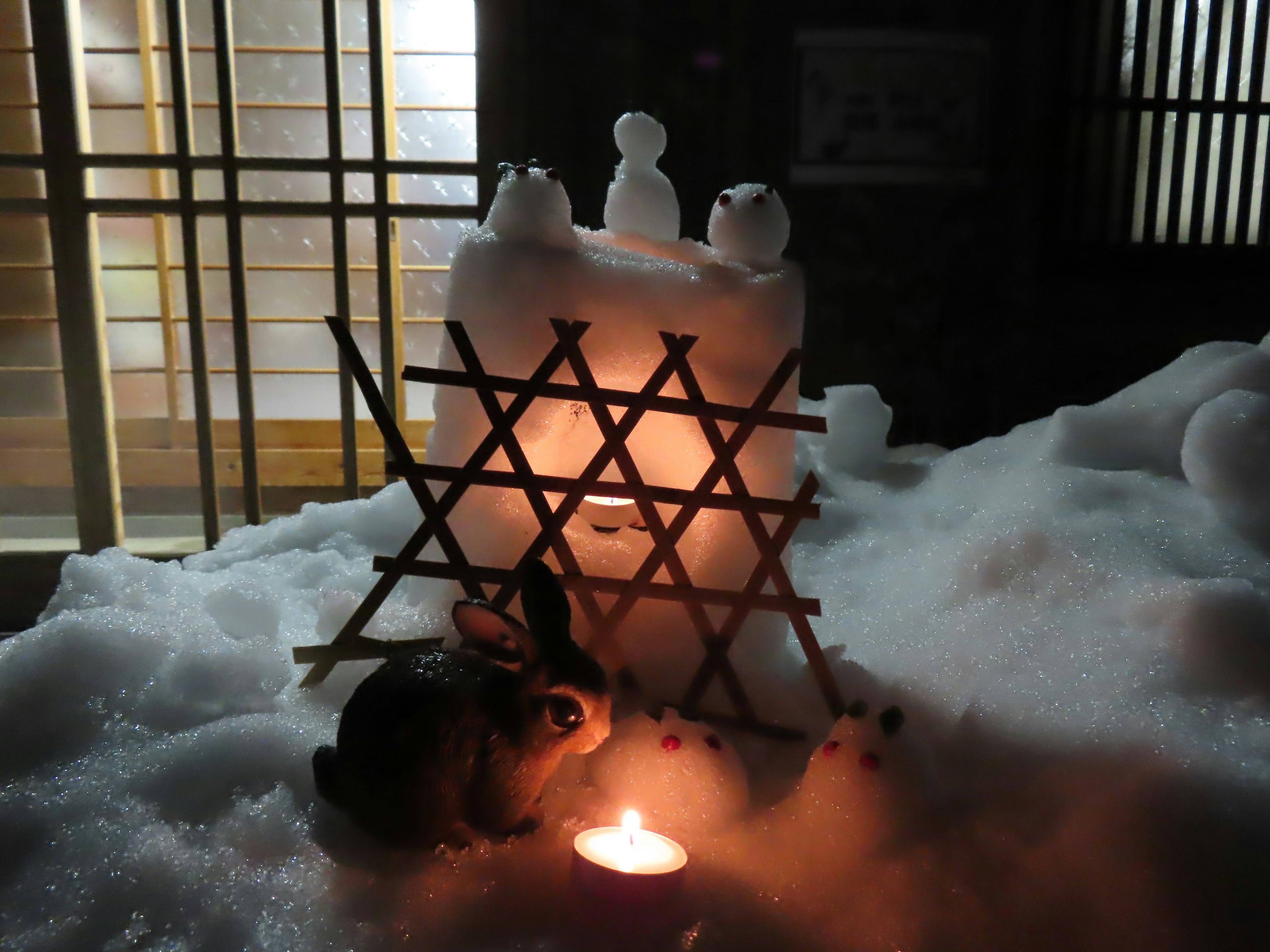 A rabbit near a candlelight surrounded by snow sculptures