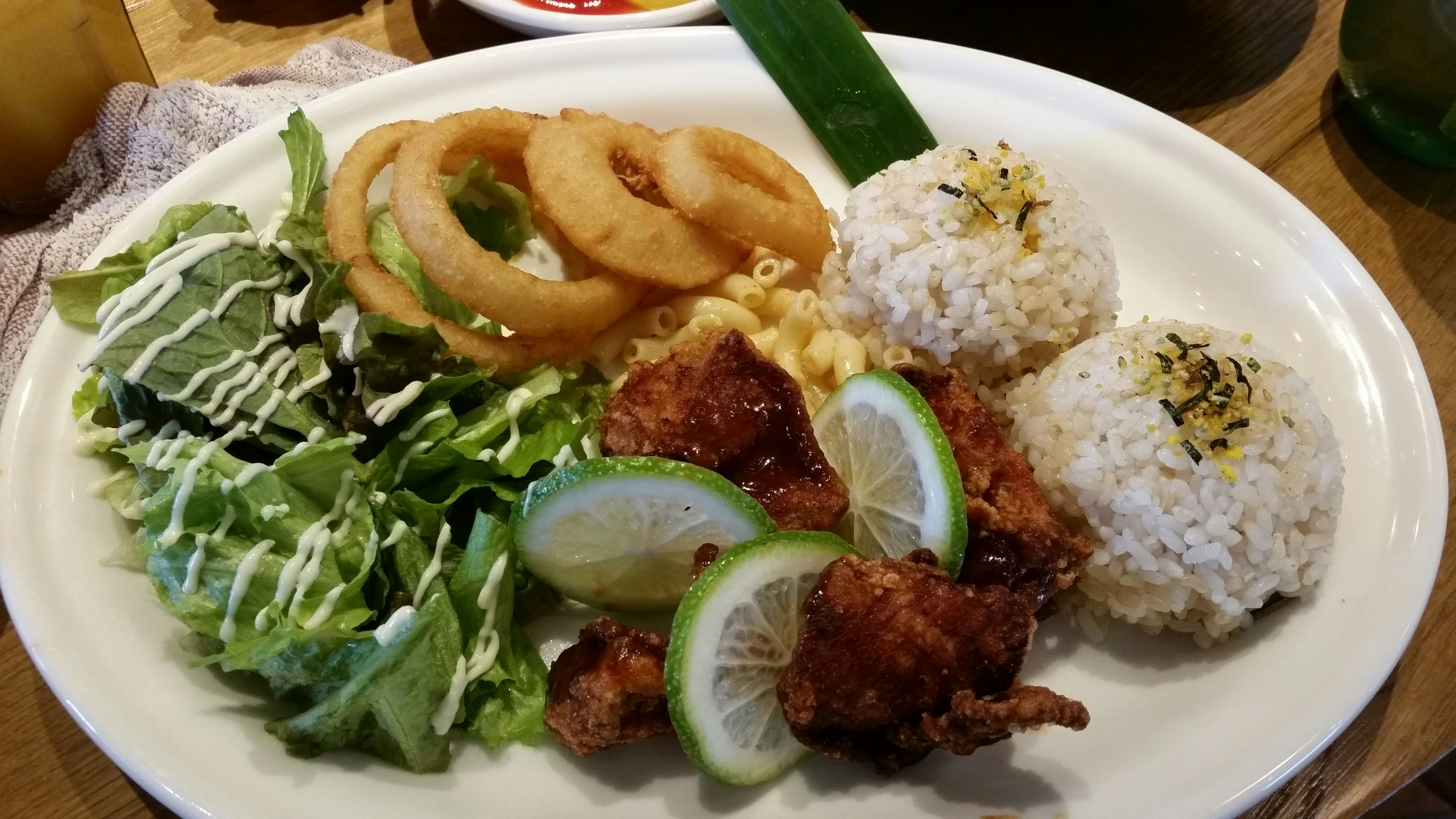 A delicious plate featuring chicken, rice, salad, onion rings, and lime slices