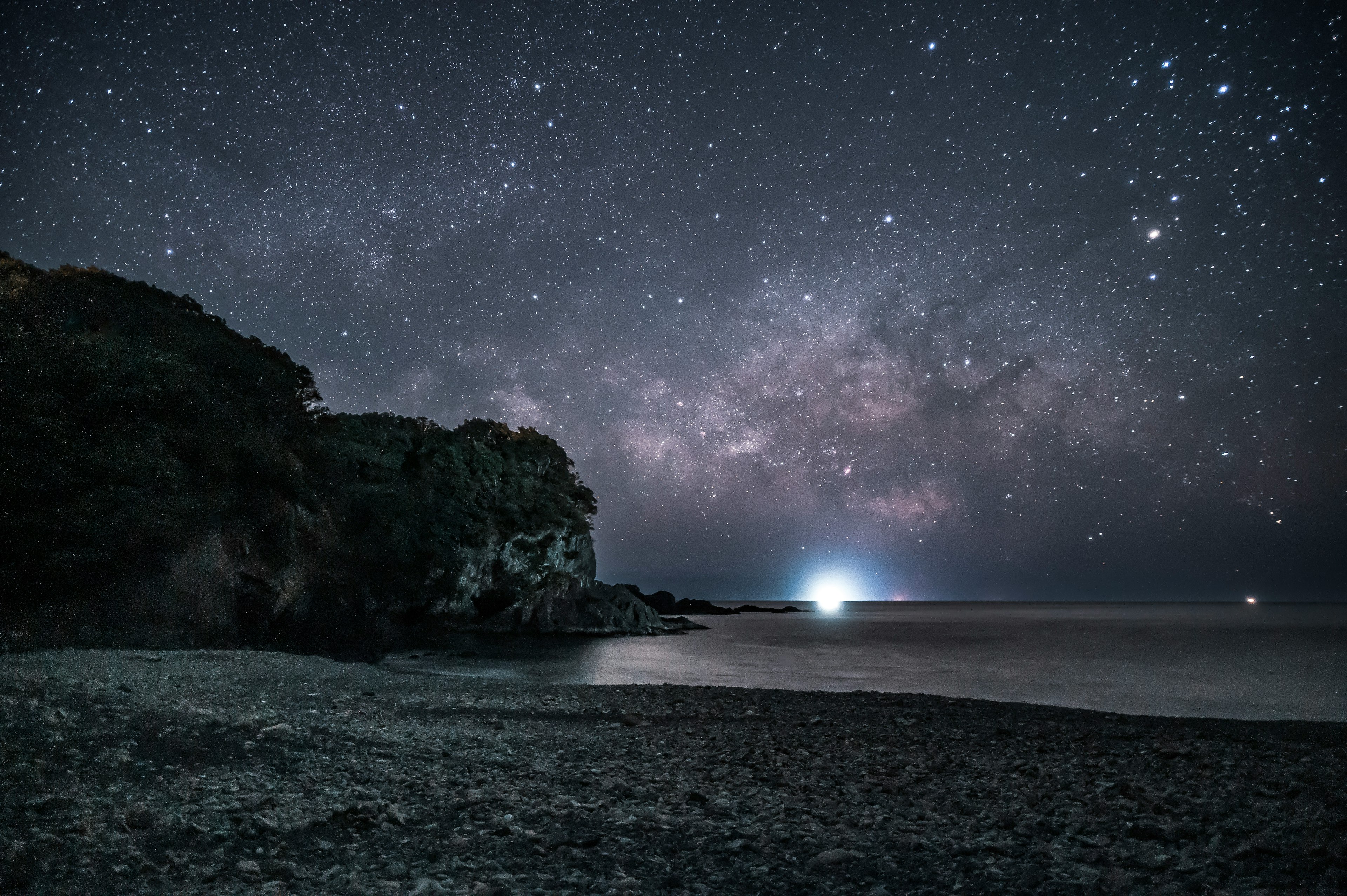 Coastal scene under a starry sky with a glowing lighthouse