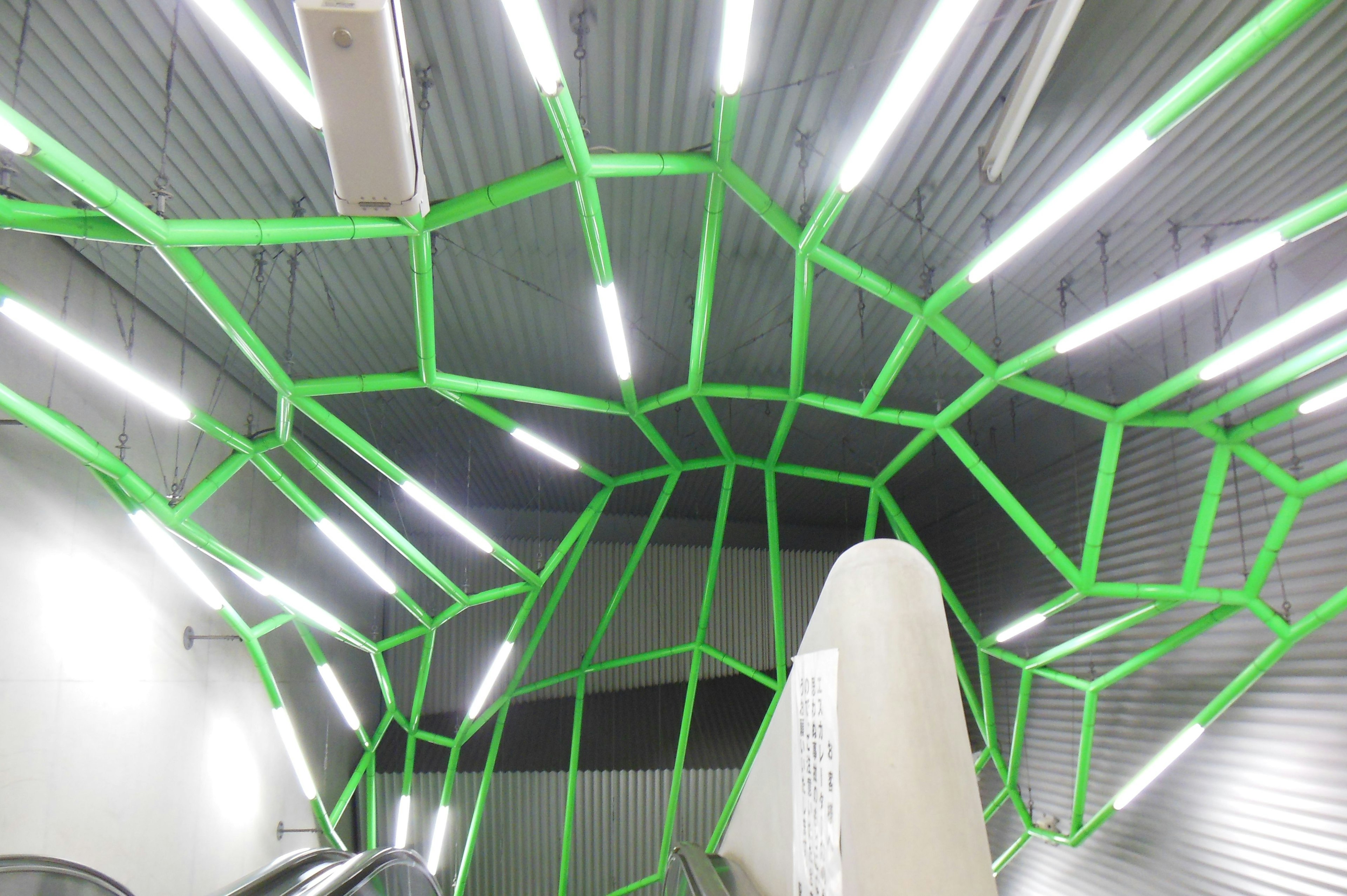 Diseño moderno del techo con líneas verdes sobre una escalera mecánica en una estación