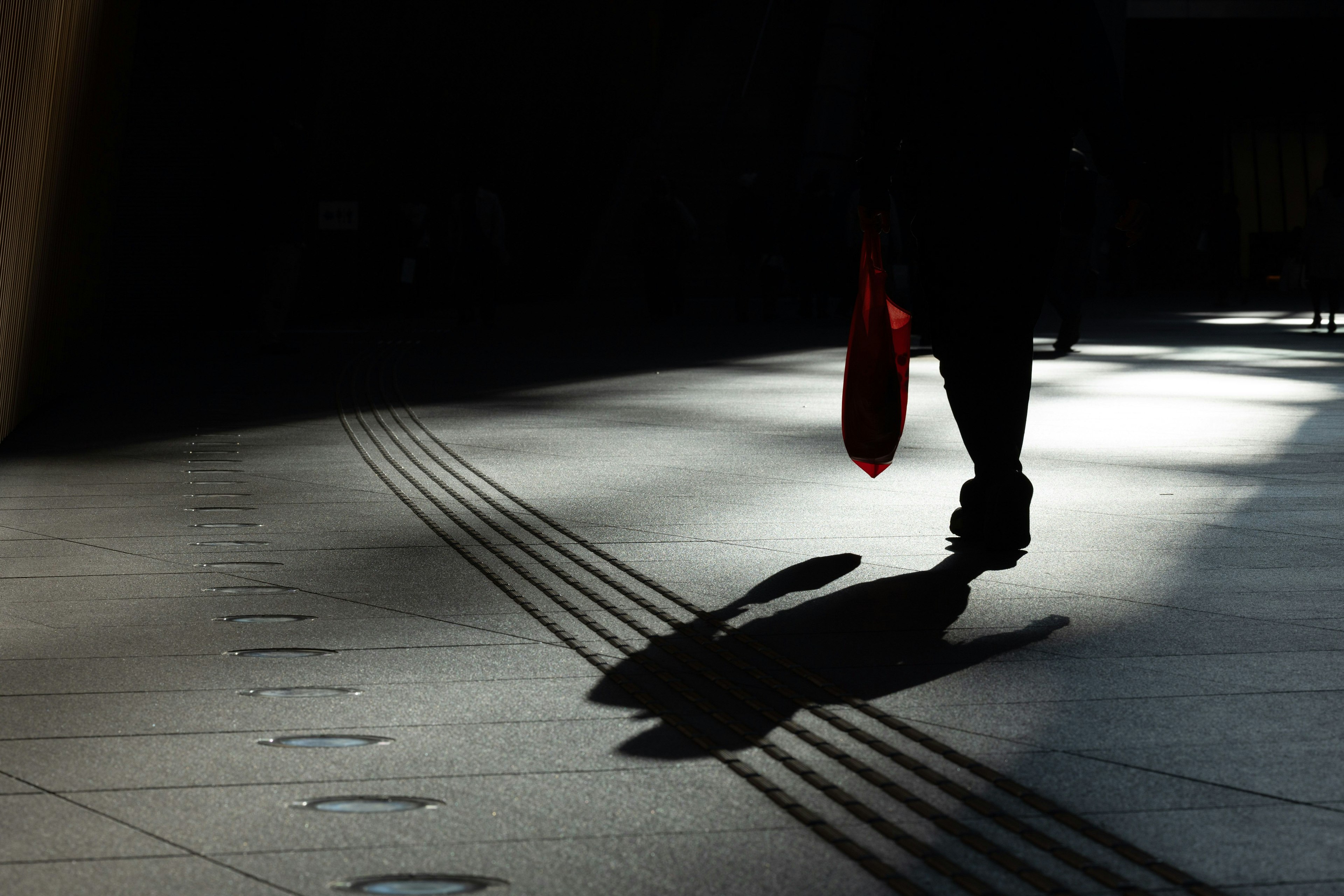 Silhouette seseorang yang berjalan dengan payung merah yang memproyeksikan bayangan di tanah