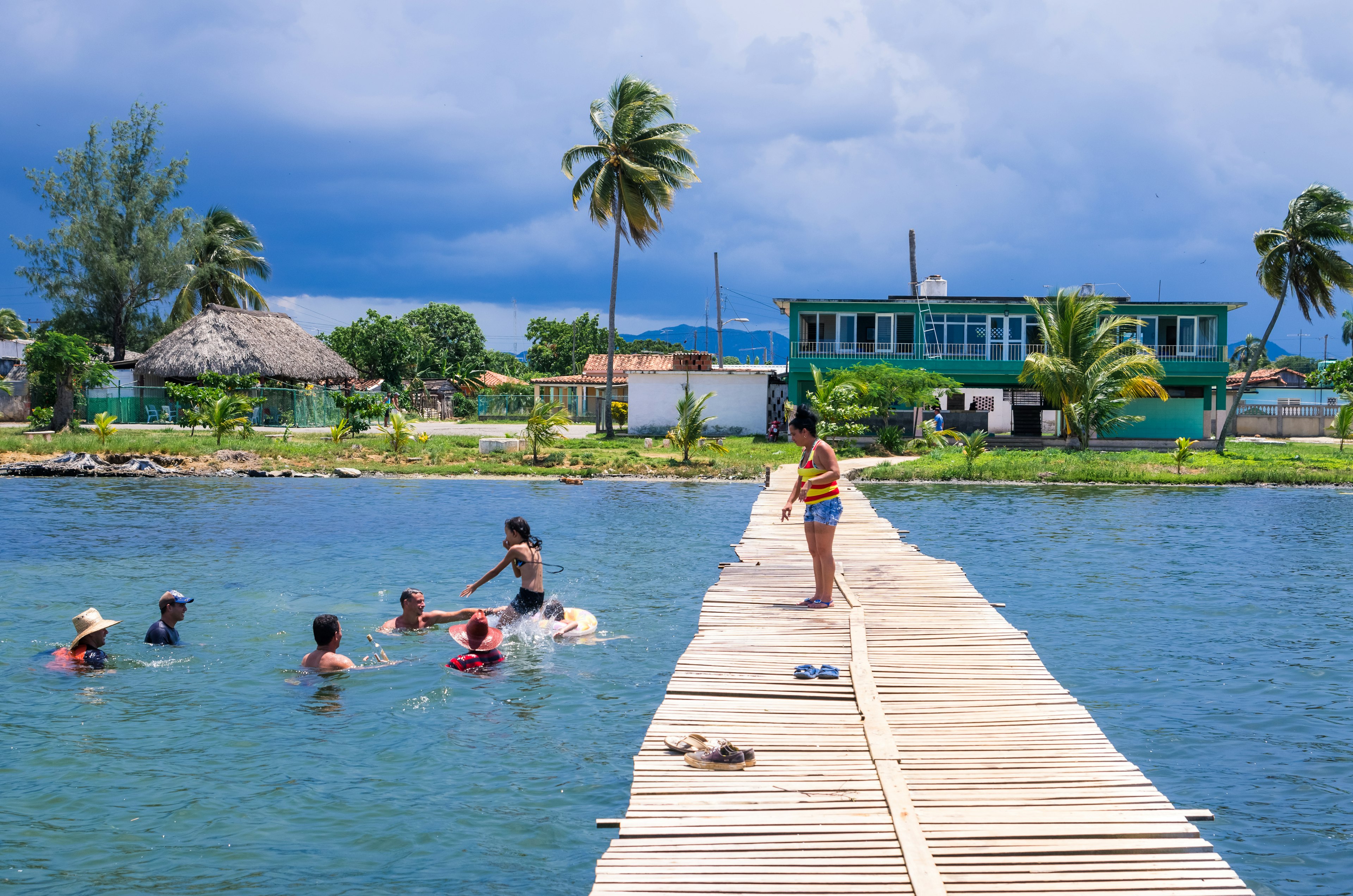 People enjoying the water near a wooden pier with palm trees in the background