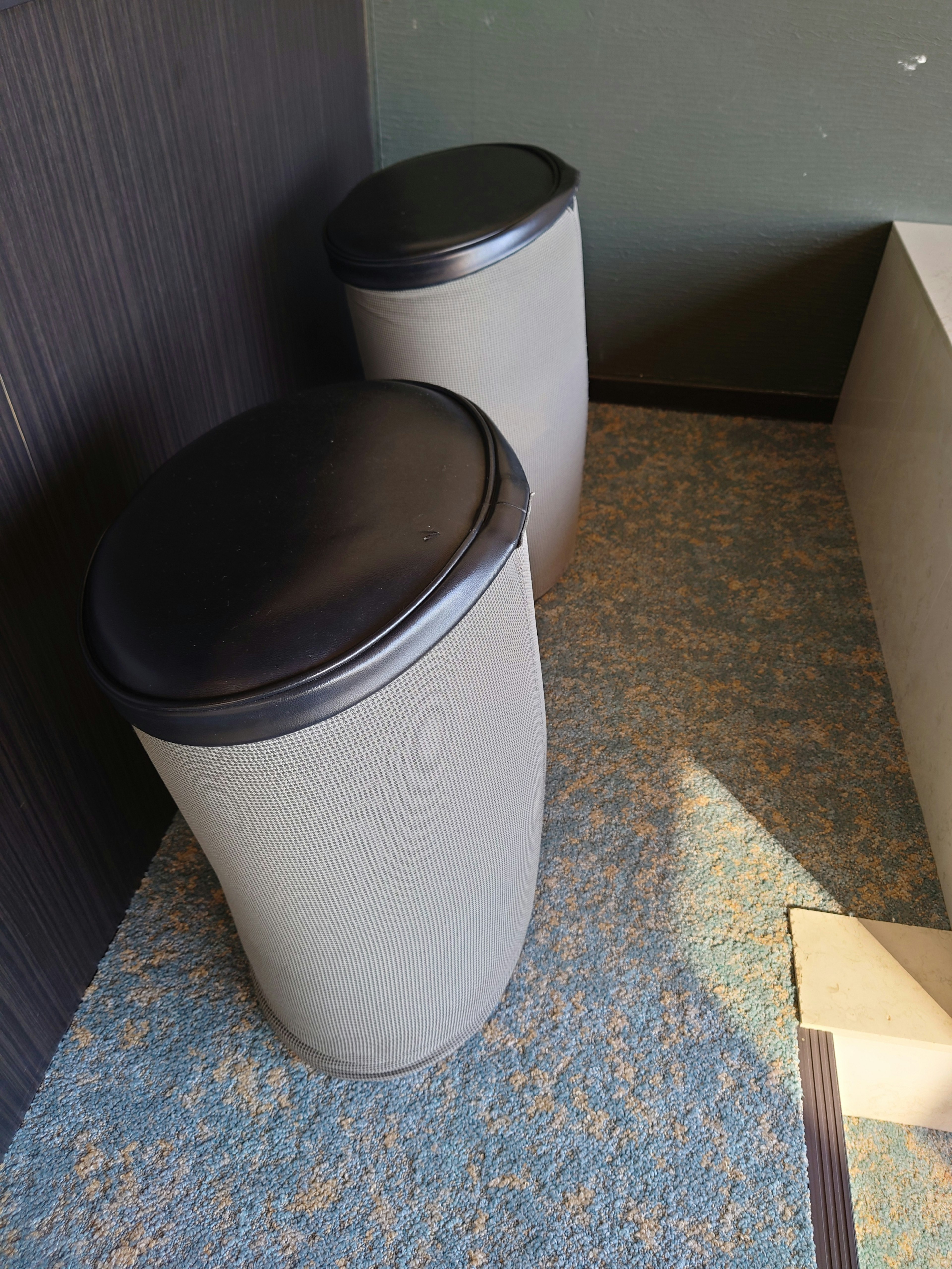 Two cylindrical trash bins with black lids in an indoor setting