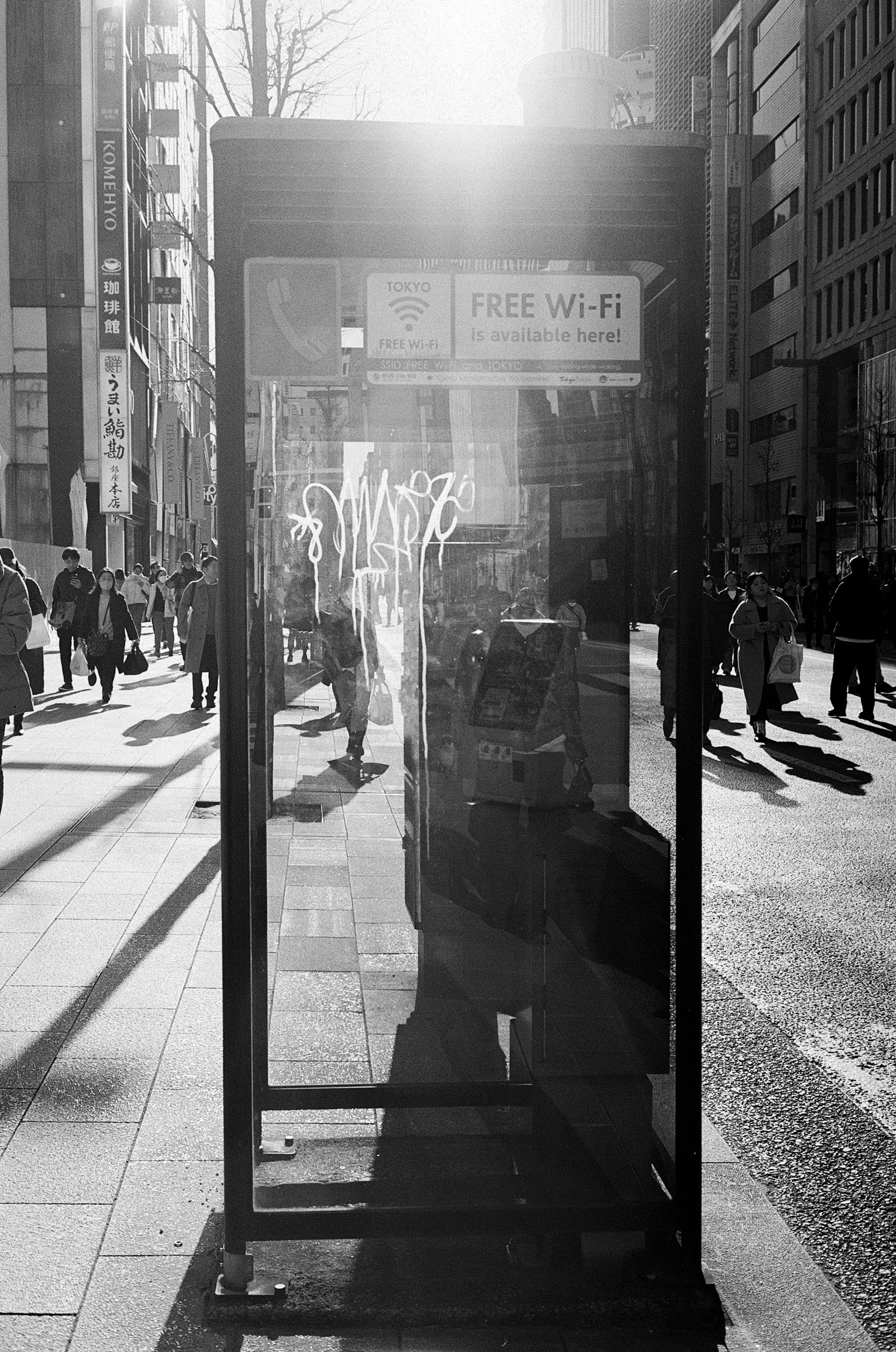 A telephone booth stands on a city street sunlight reflecting creating a striking black and white contrast