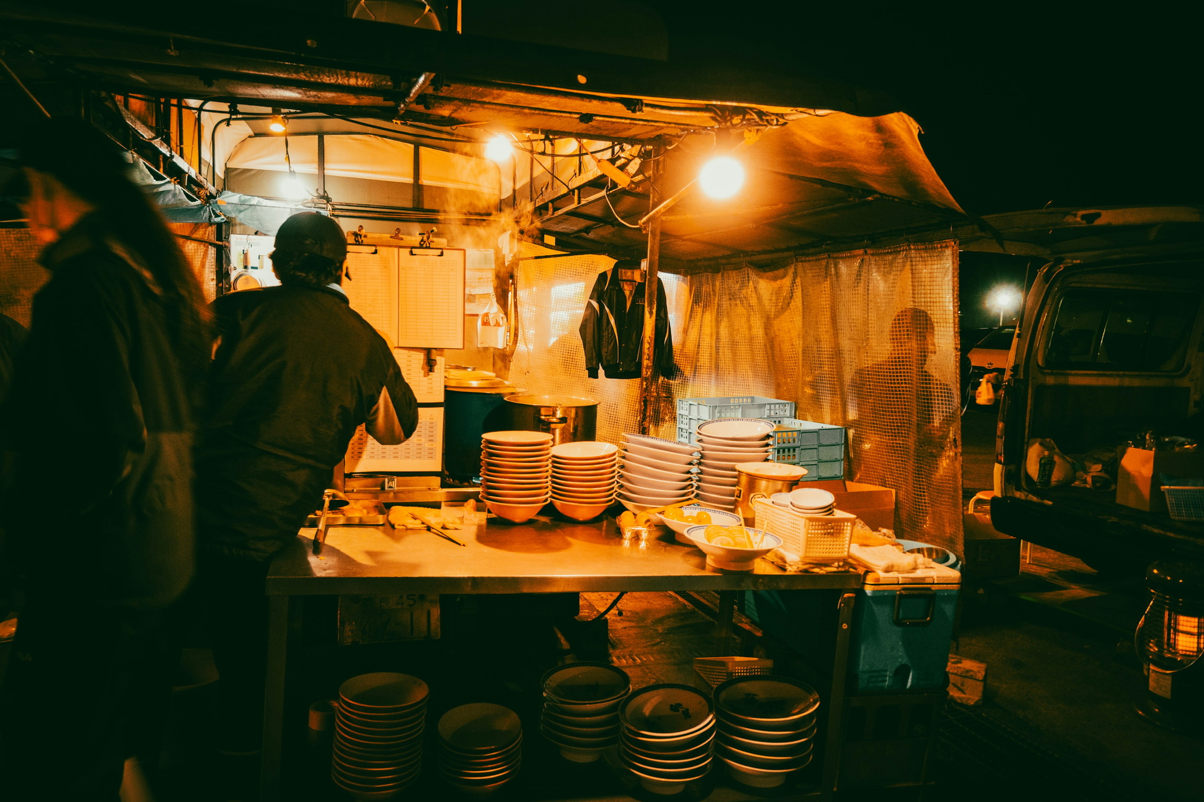 Puesto de mercado nocturno con una persona cocinando y platos apilados en una mesa