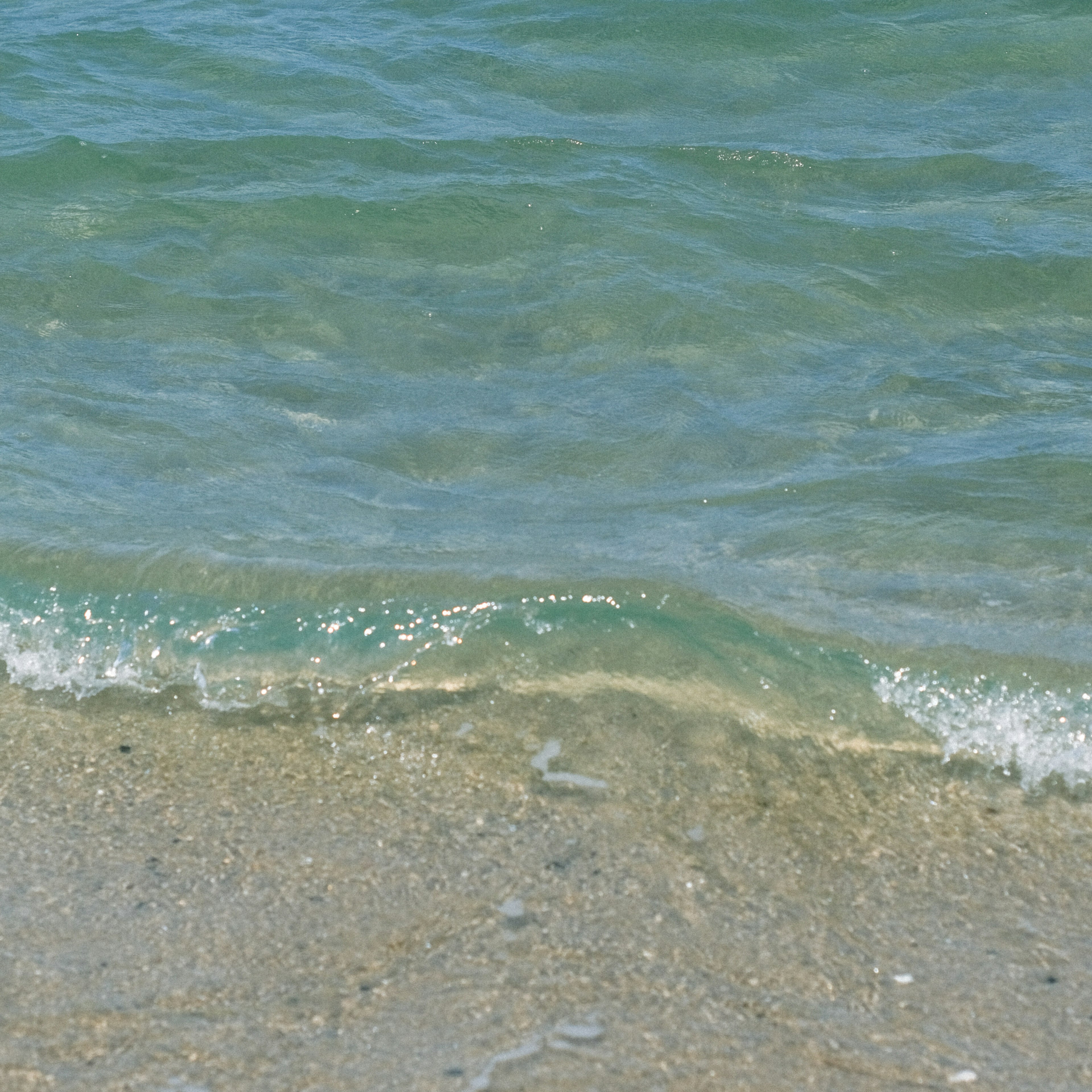 Sanfte Wellen brechen an einem klaren blauen Meer und einem Sandstrand