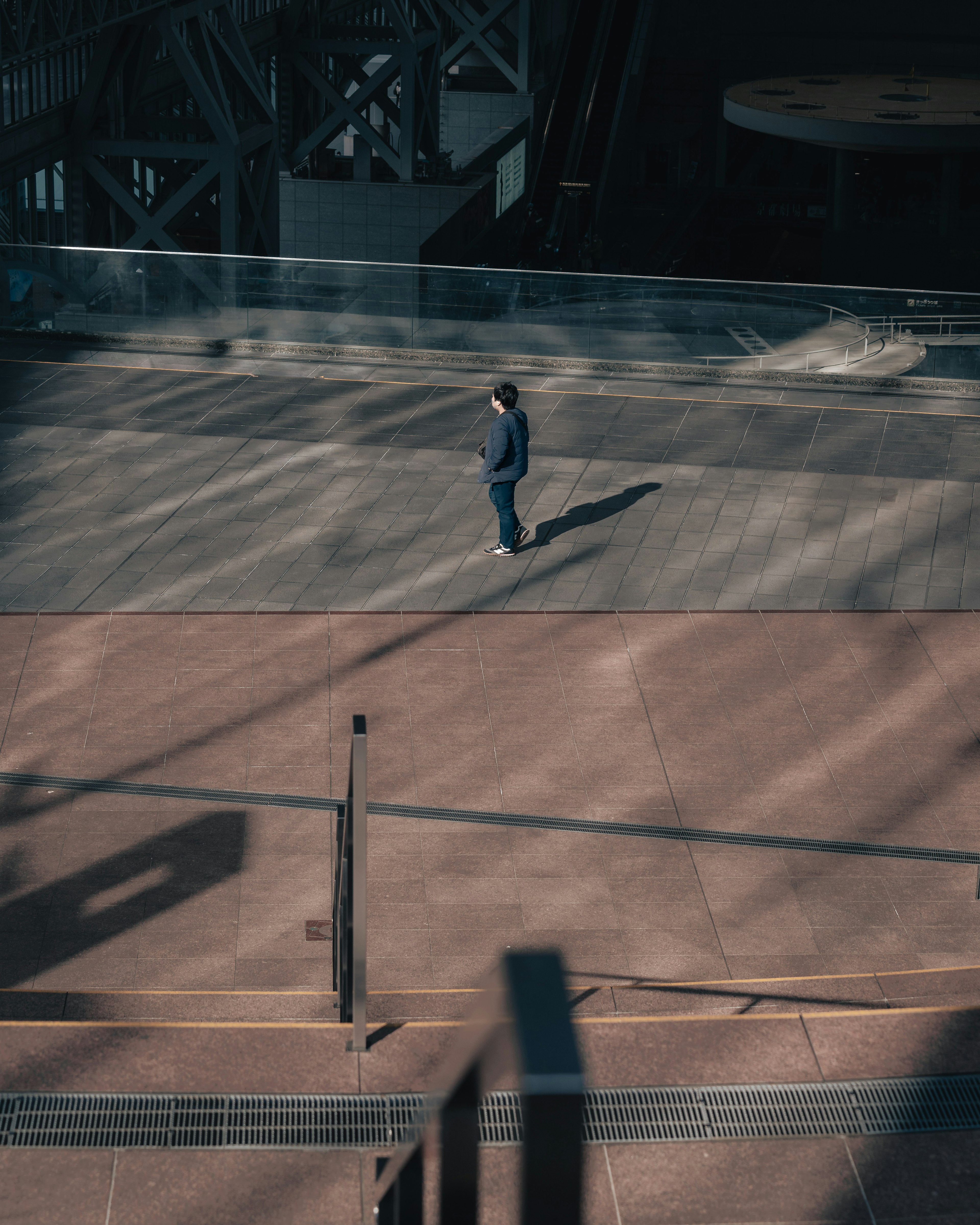 A person in blue clothing walking on a shadowed paved path