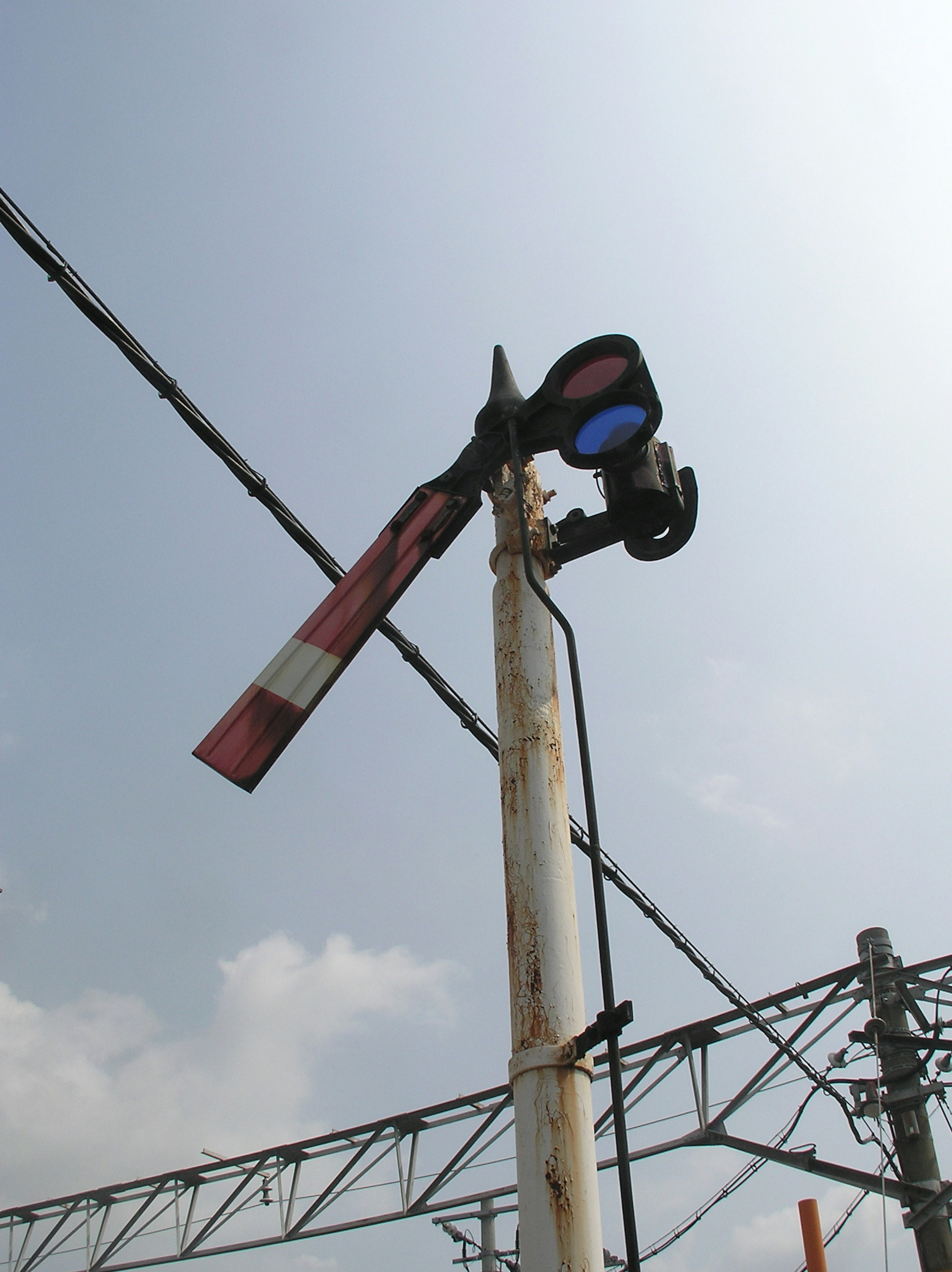 Railroad signal with blue light and red-white gate arm against a clear sky