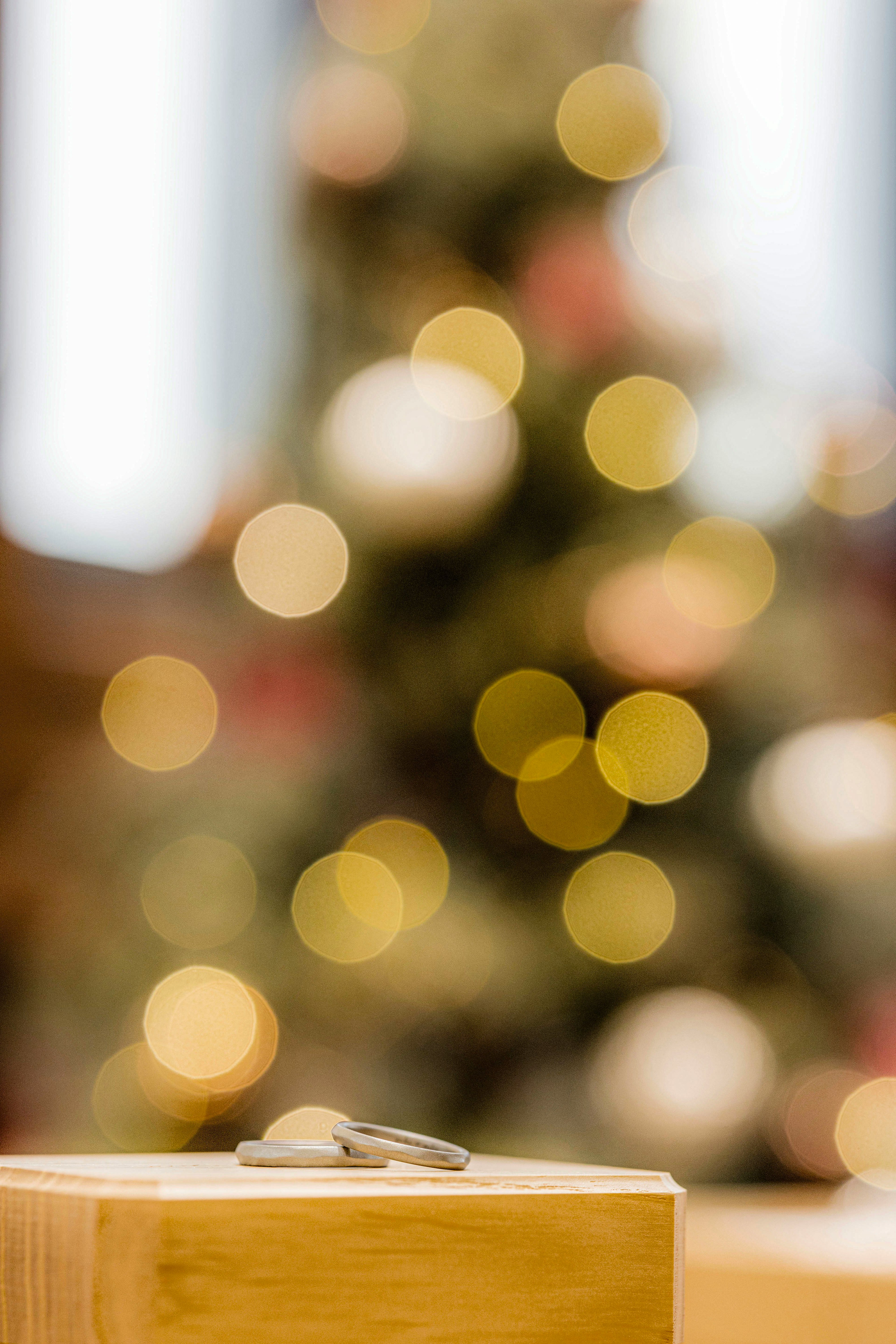 A wedding ring placed on a wooden surface with a softly blurred Christmas tree in the background