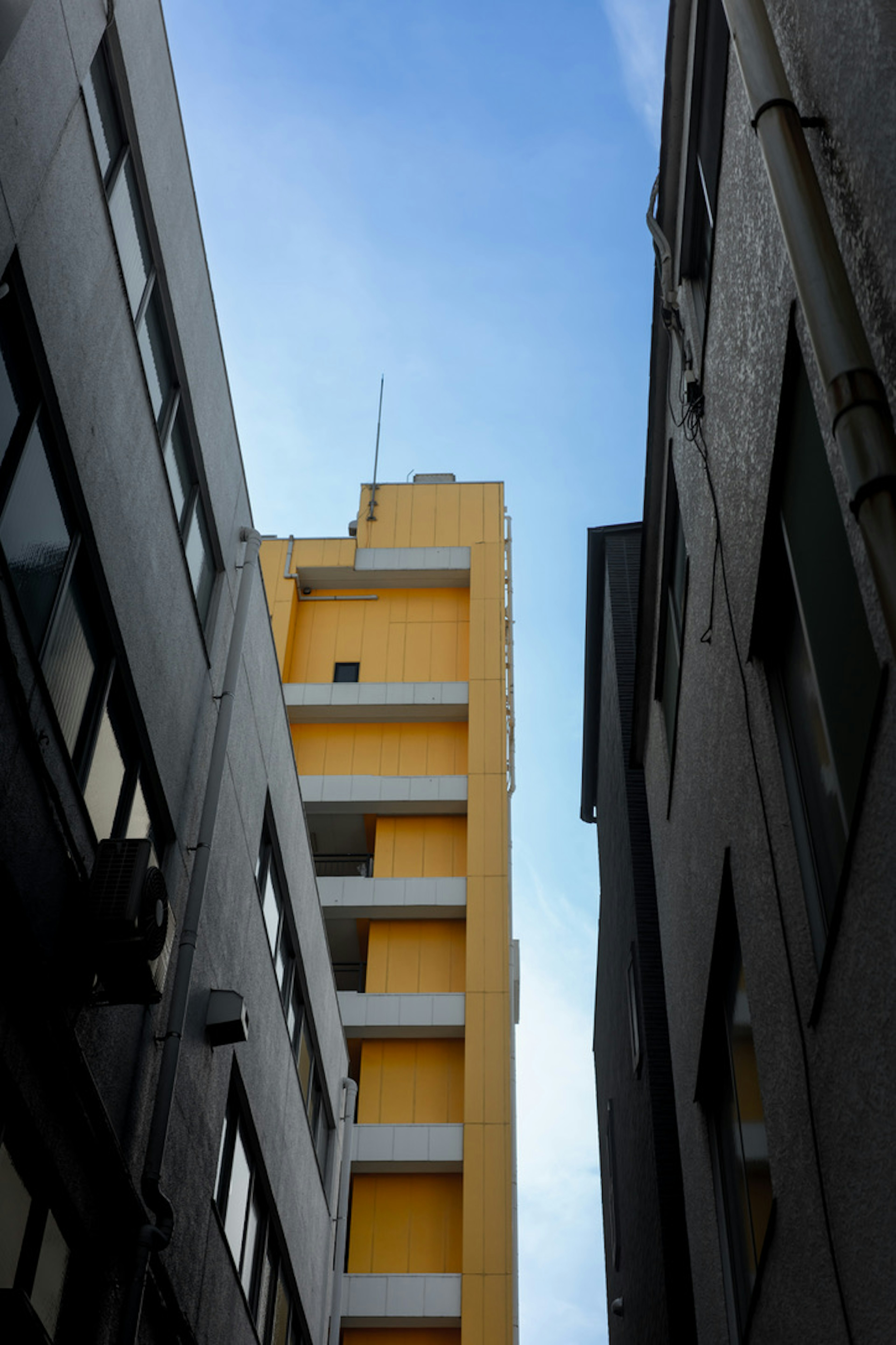 Gelbes Gebäude zwischen zwei grauen Gebäuden unter einem blauen Himmel sichtbar