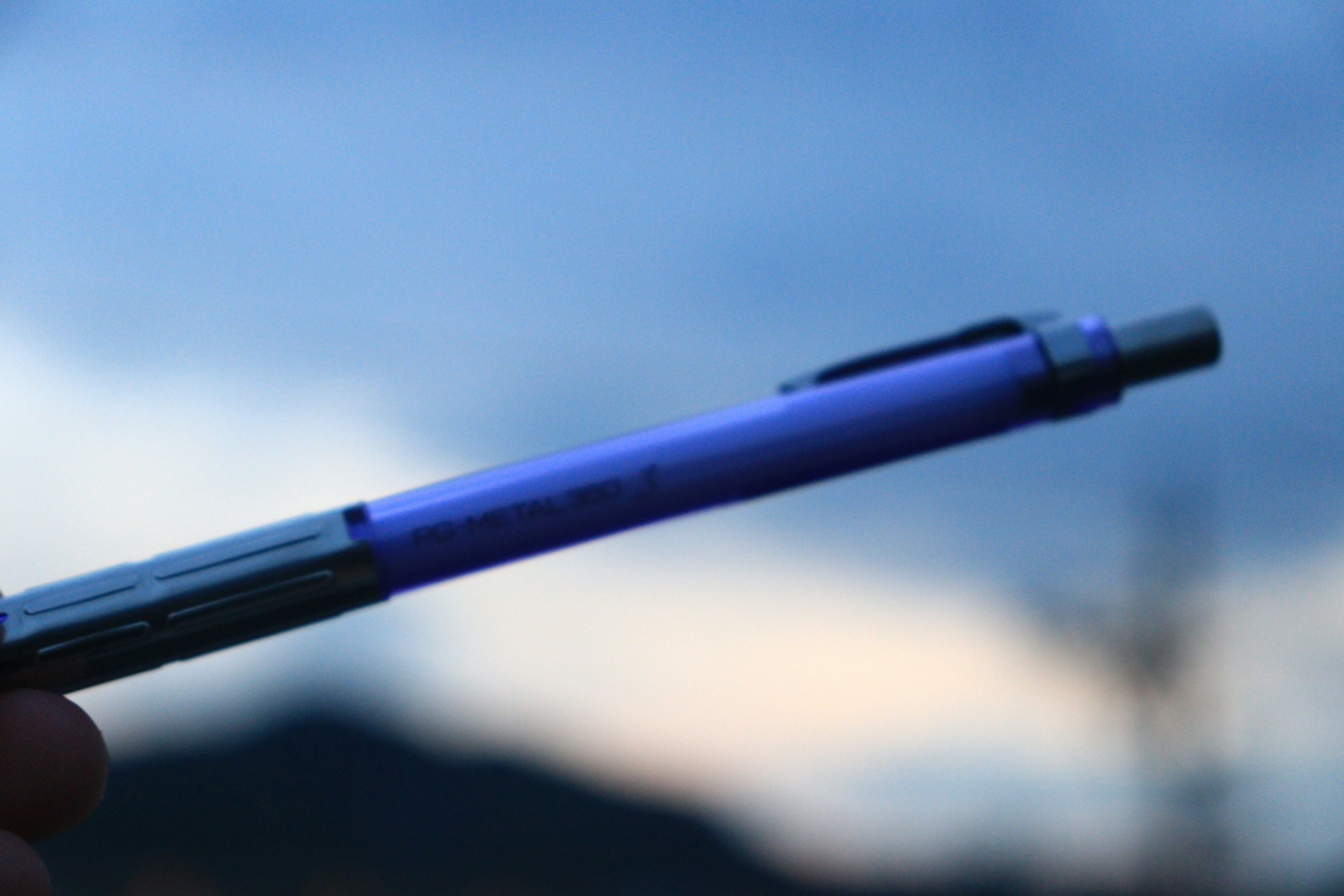 A blue-purple pen held in hand with a sunset sky in the background