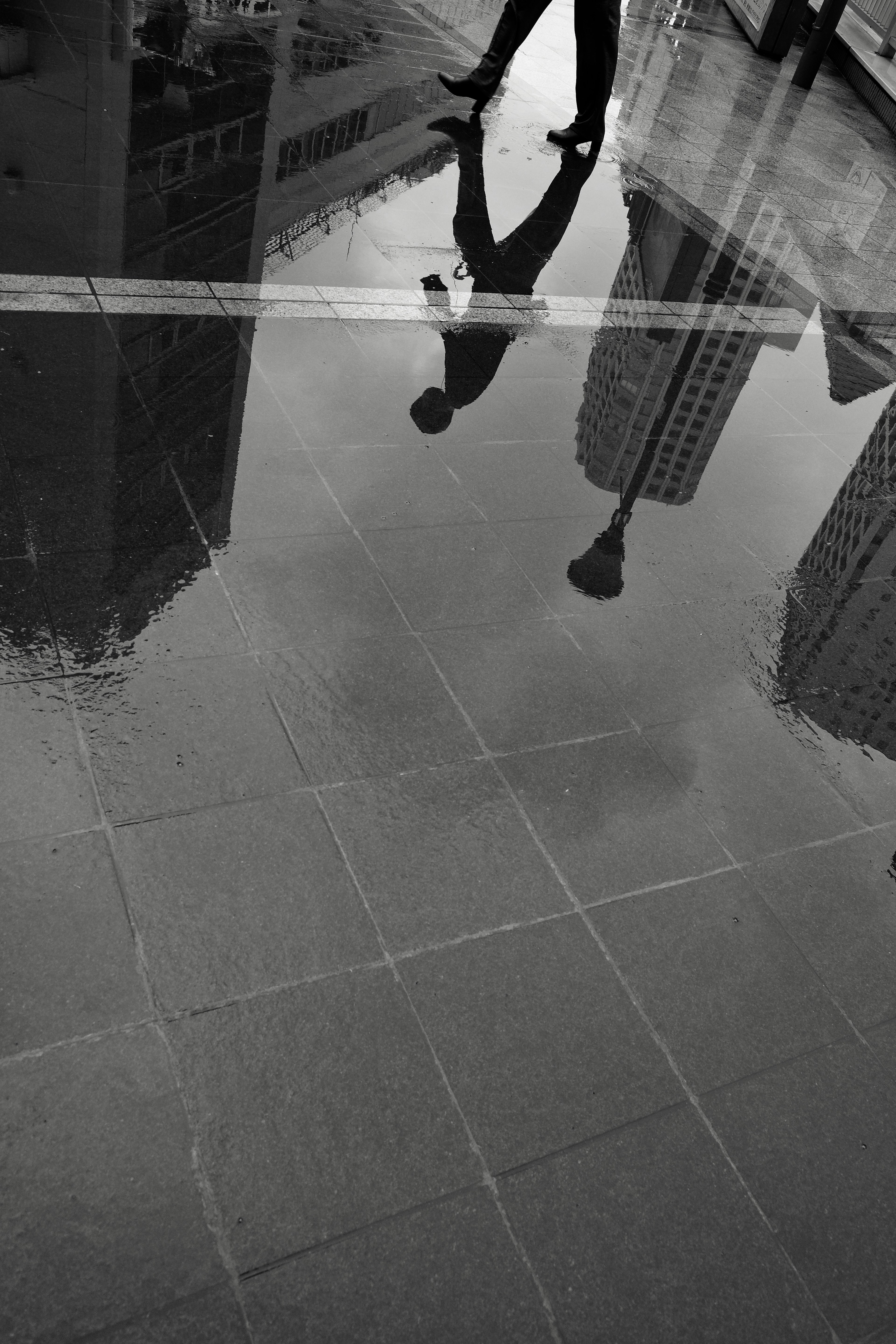 Black and white photo of a person walking reflected in a puddle in the city