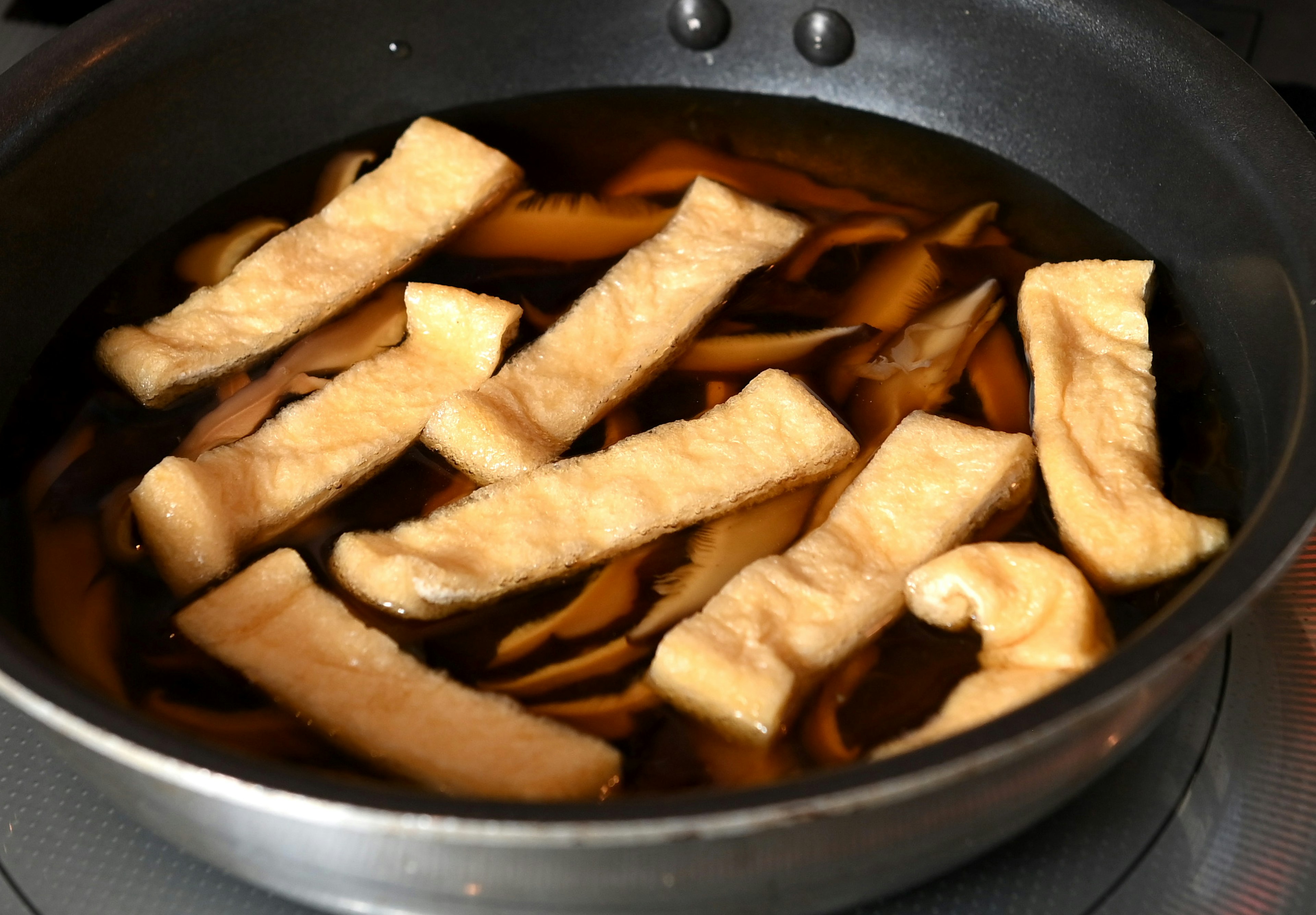 Rectangular pieces of fried tofu simmering in a pot