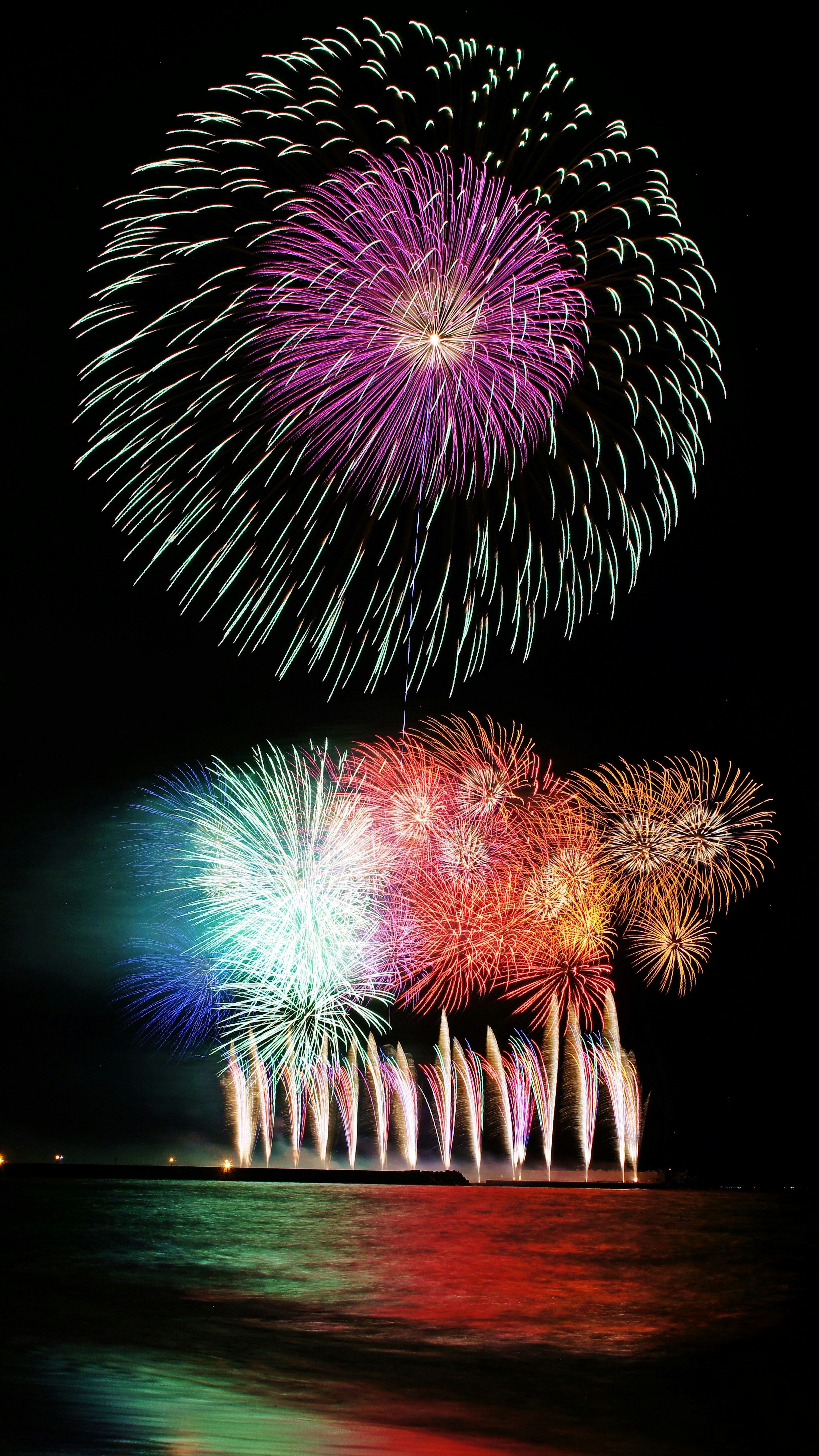 Fuegos artificiales coloridos estallando en el cielo nocturno con reflejos en el agua