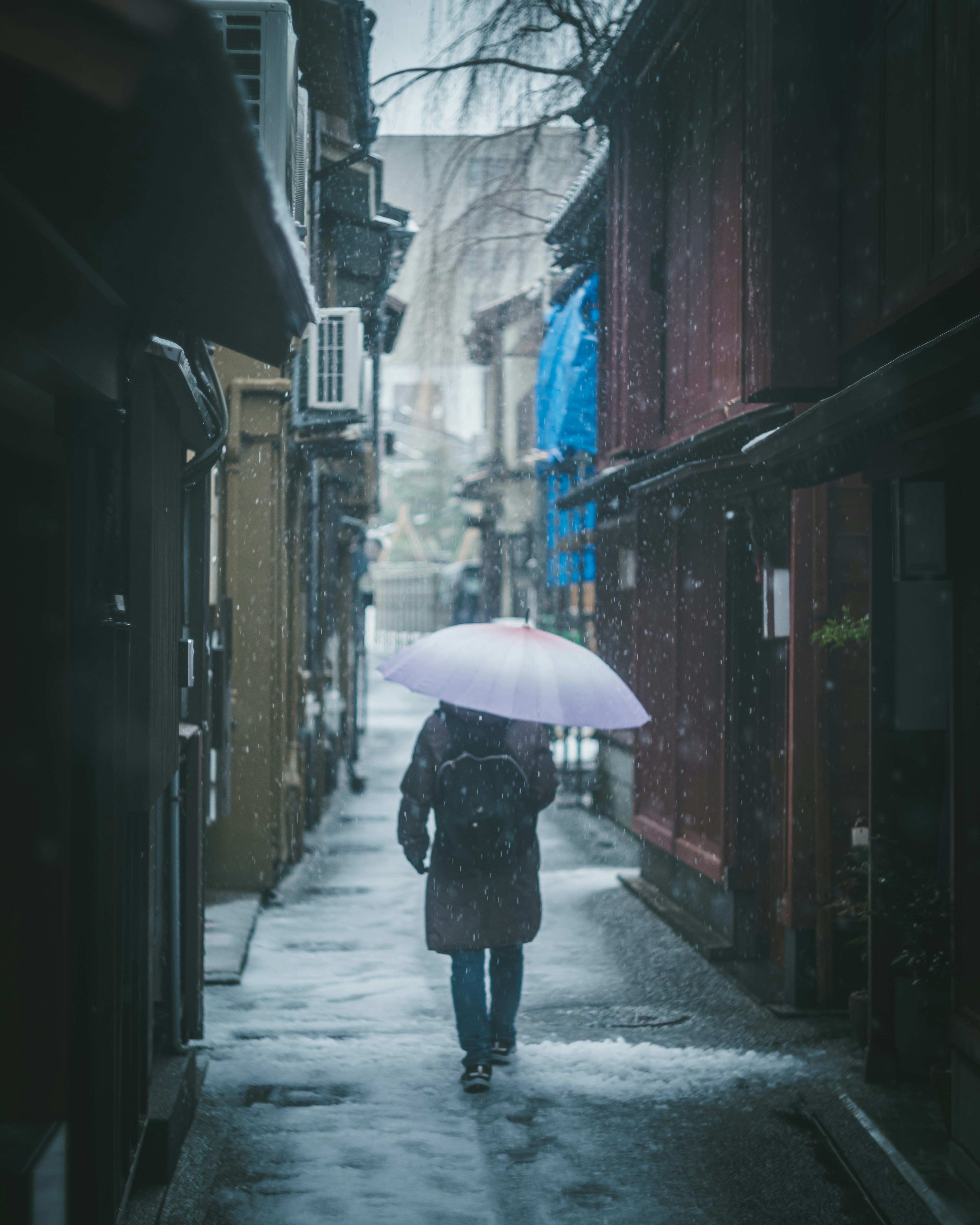 A person walking in a narrow alley holding an umbrella in the rain