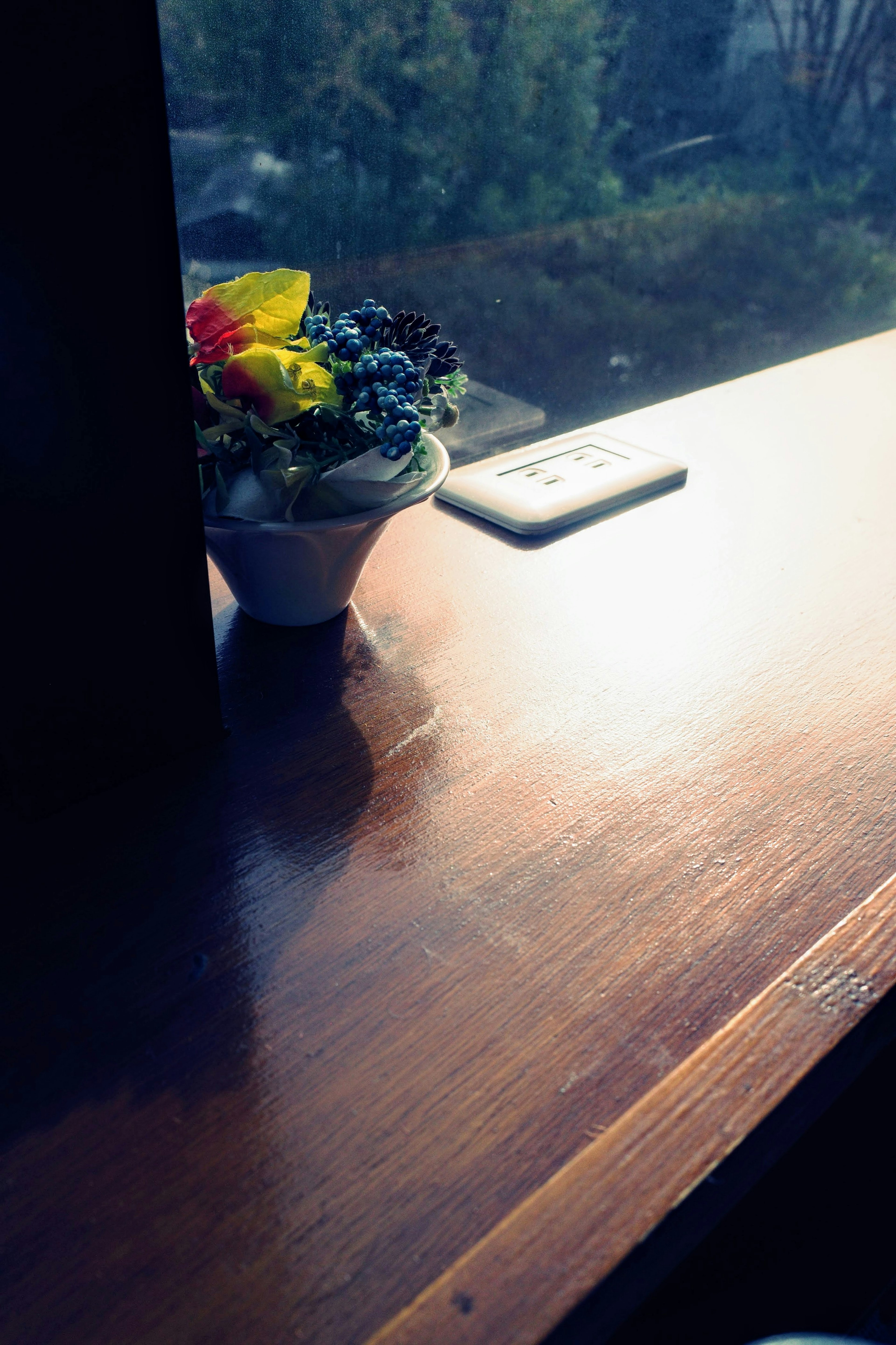 Mesa de madera junto a la ventana con una maceta de flores y un teléfono inteligente