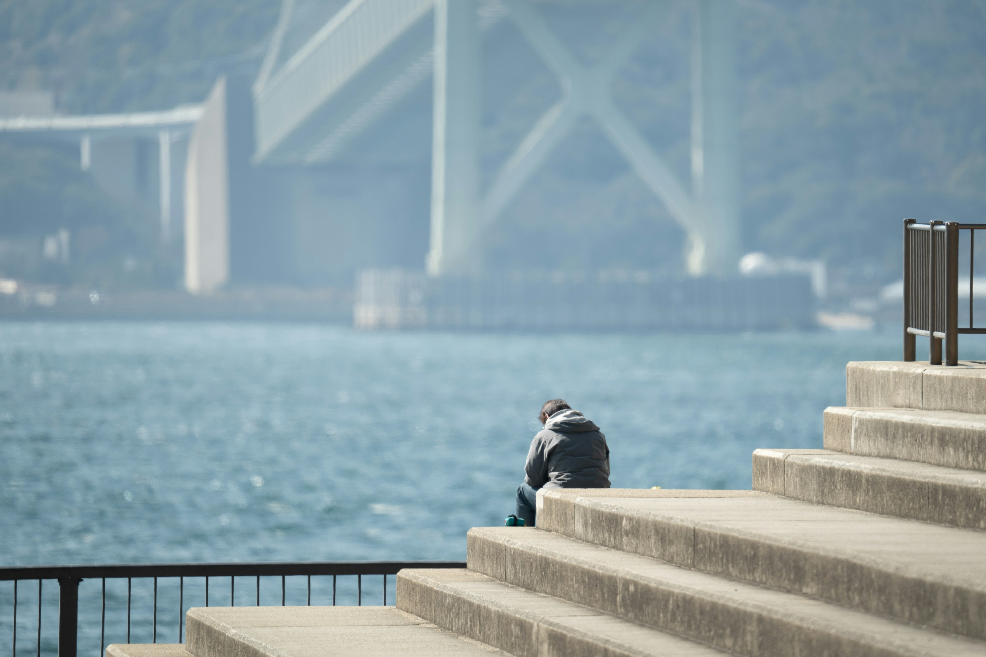 Eine Person sitzt am Wasser mit einer Brücke im Hintergrund