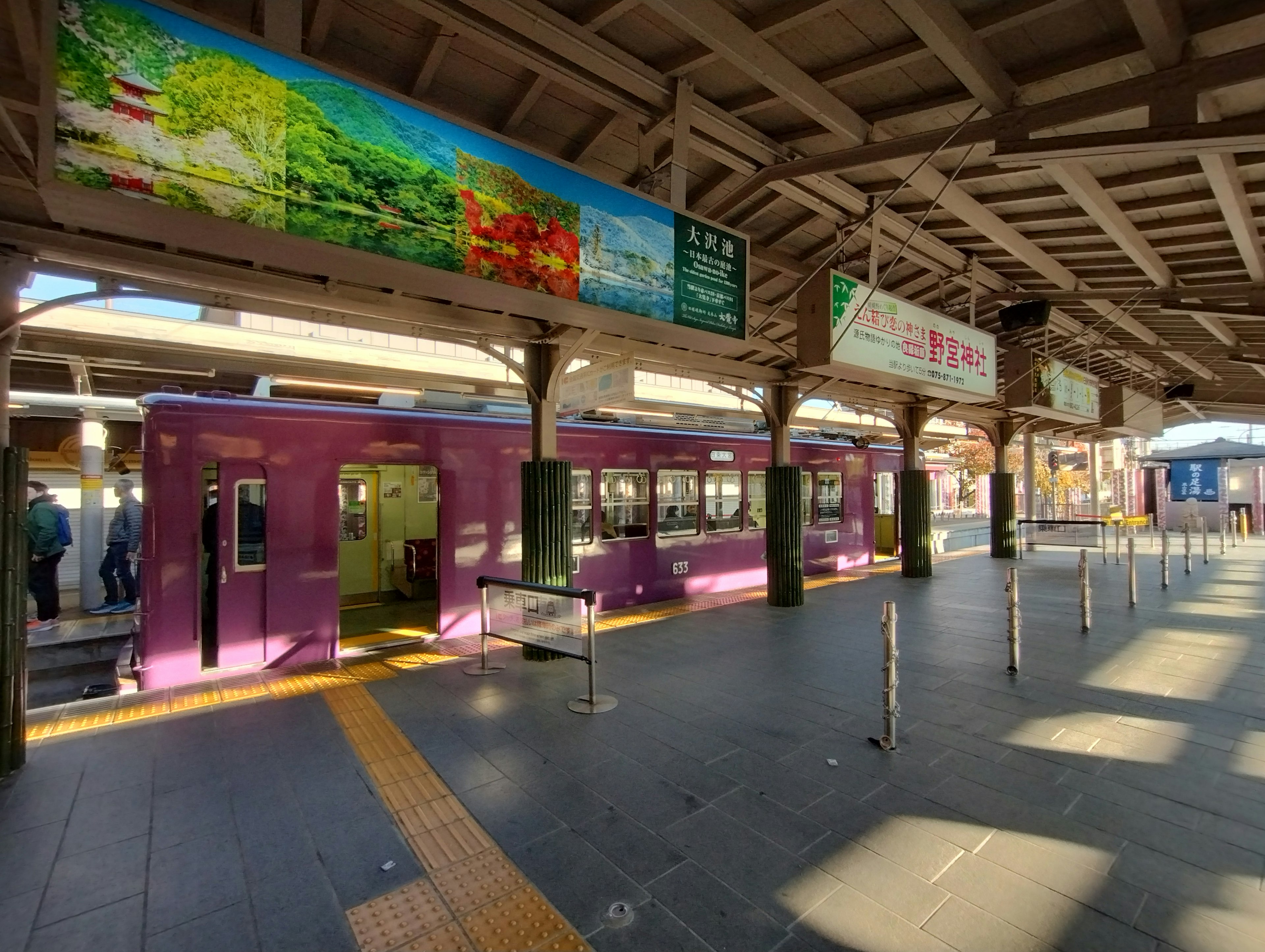 Vista de la plataforma de una estación con un tren púrpura y pancartas coloridas