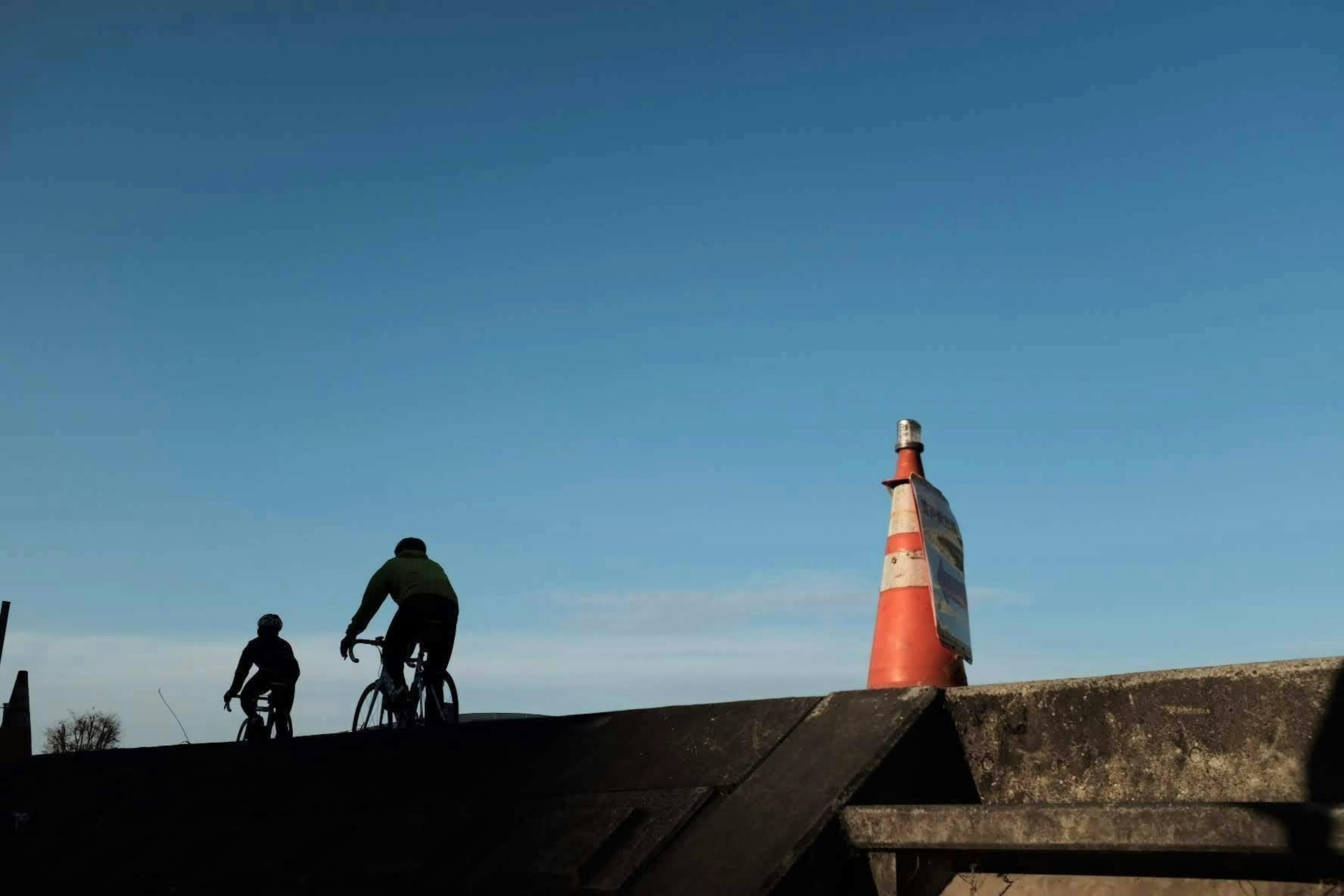 Two cyclists riding under a blue sky with an orange traffic cone