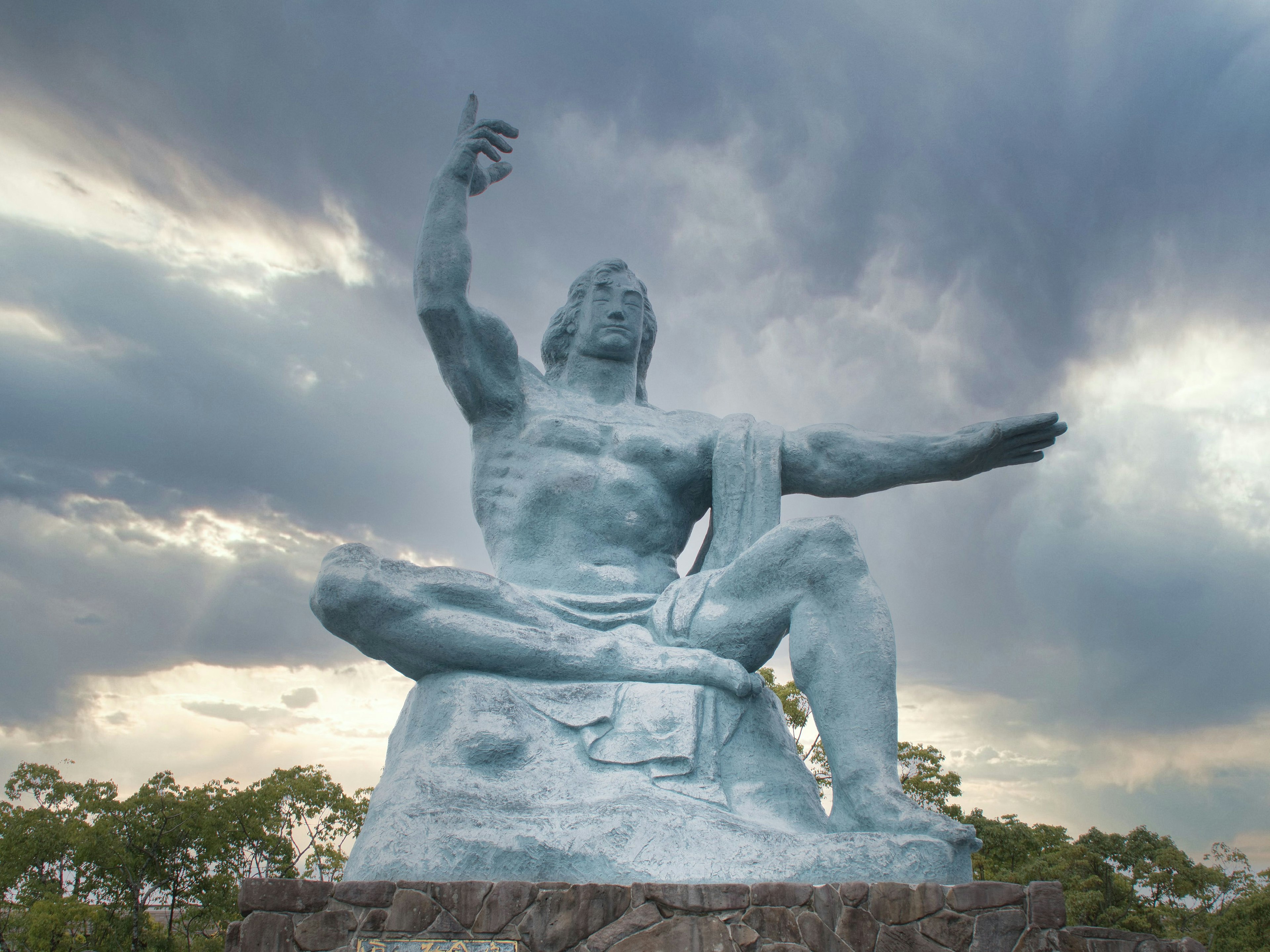 Statue en bronze avec une main levée sous un ciel nuageux