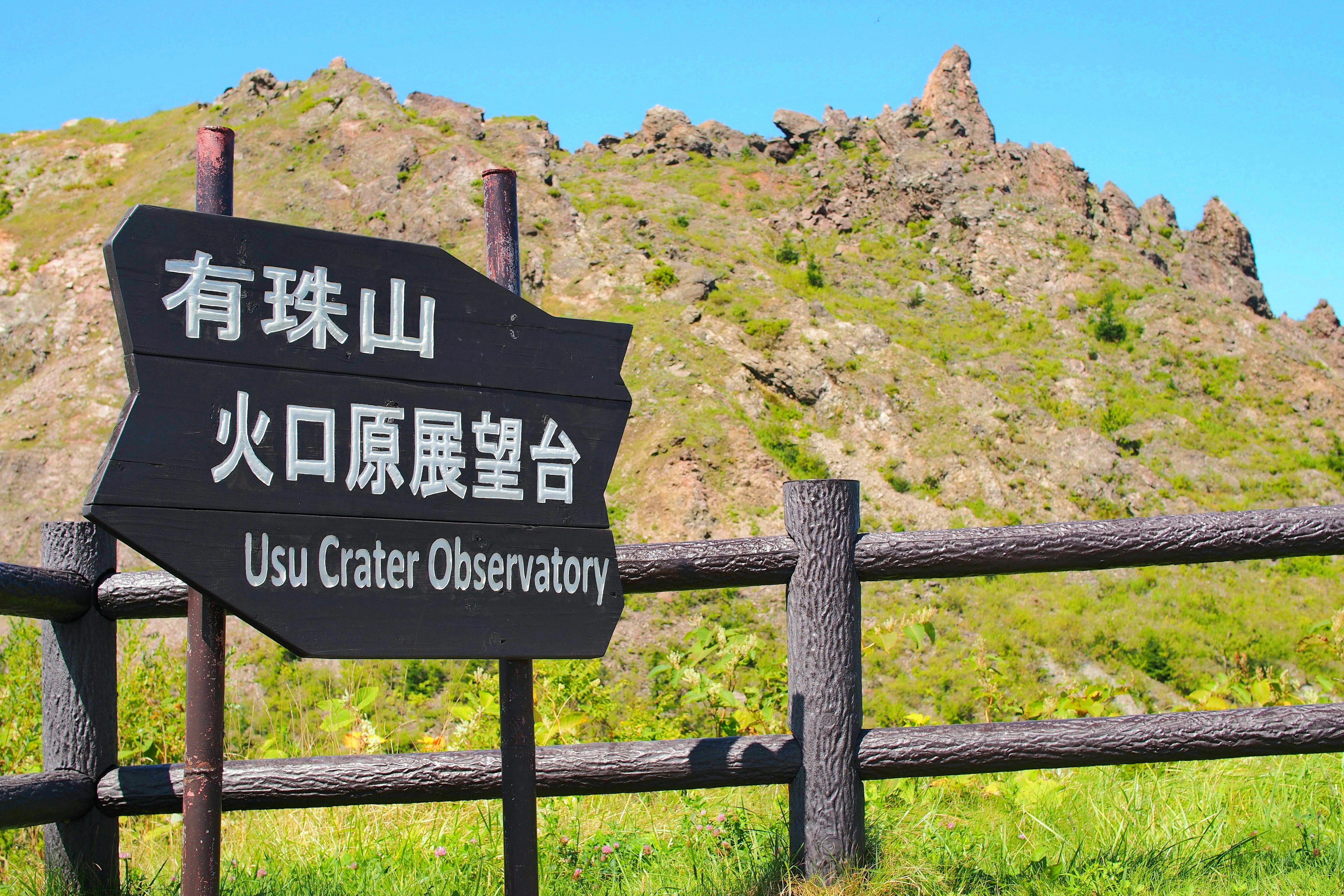 Schild für das Usu-Kraterobservatorium mit grünen Bergen im Hintergrund