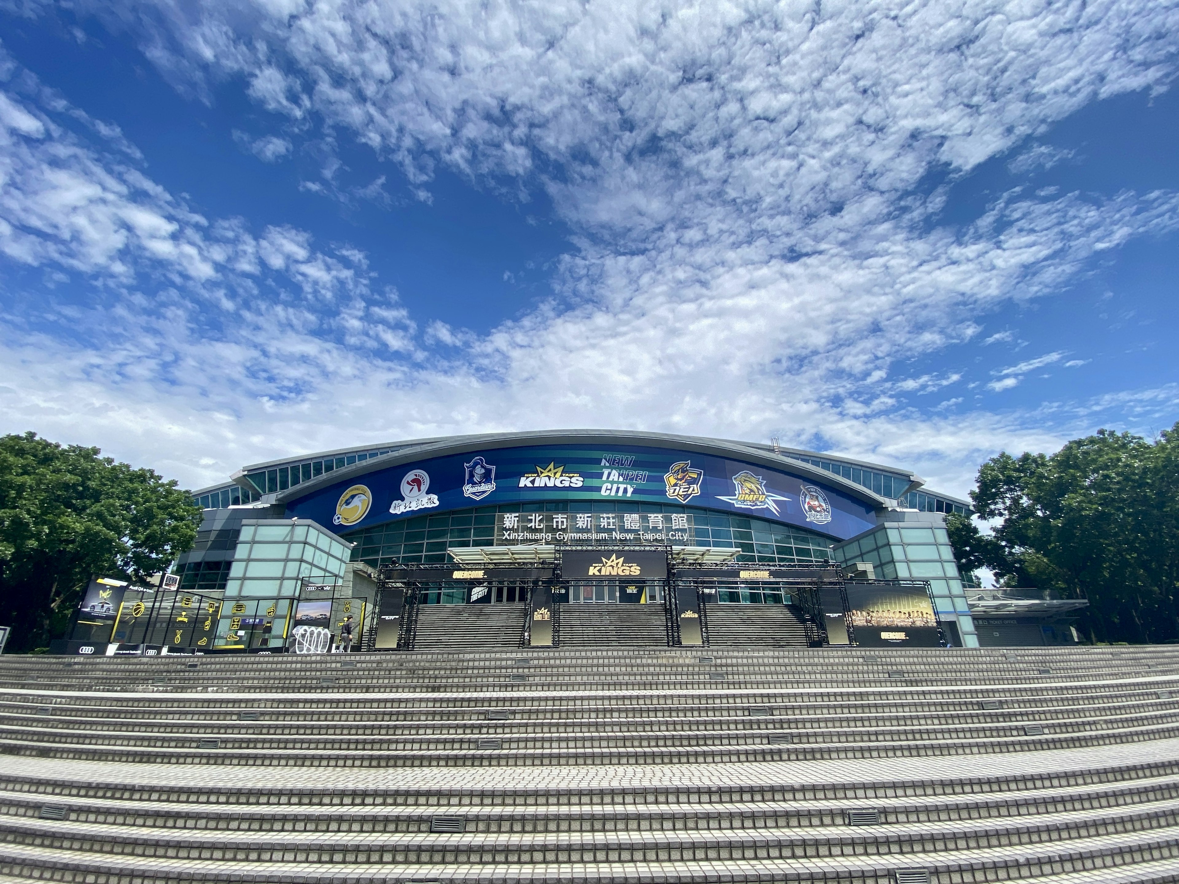 Modern building exterior under blue sky featuring large stairs and advertising banners