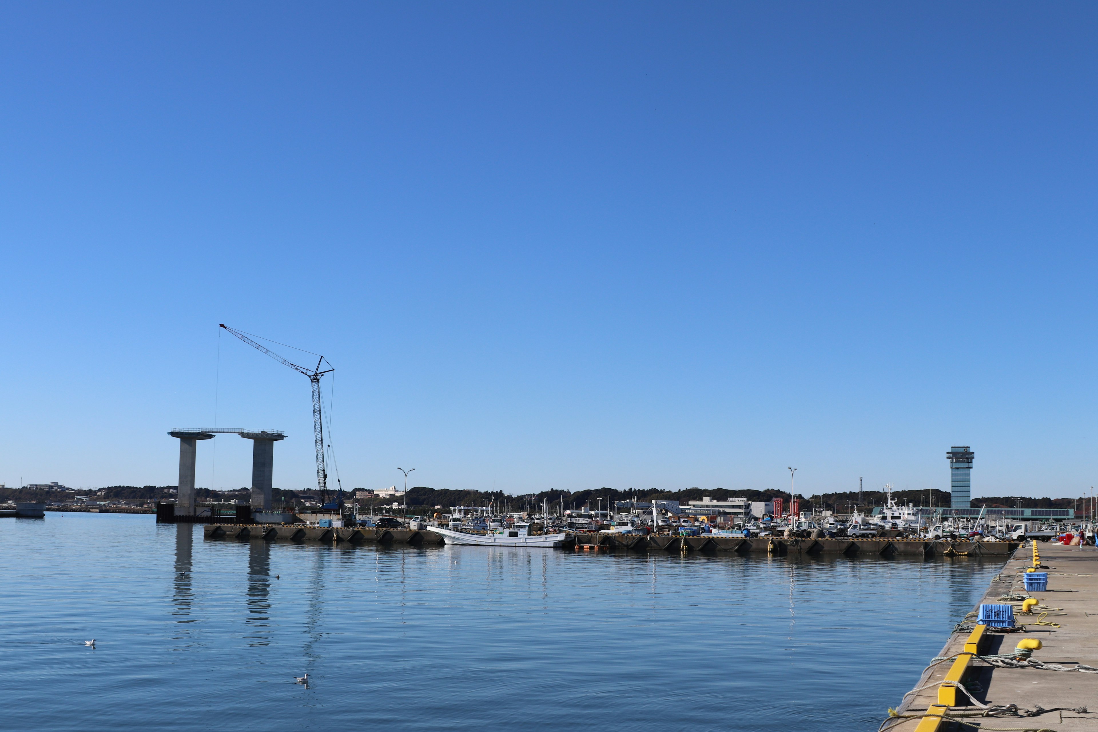 Harbor view under a clear blue sky featuring a crane and yachts