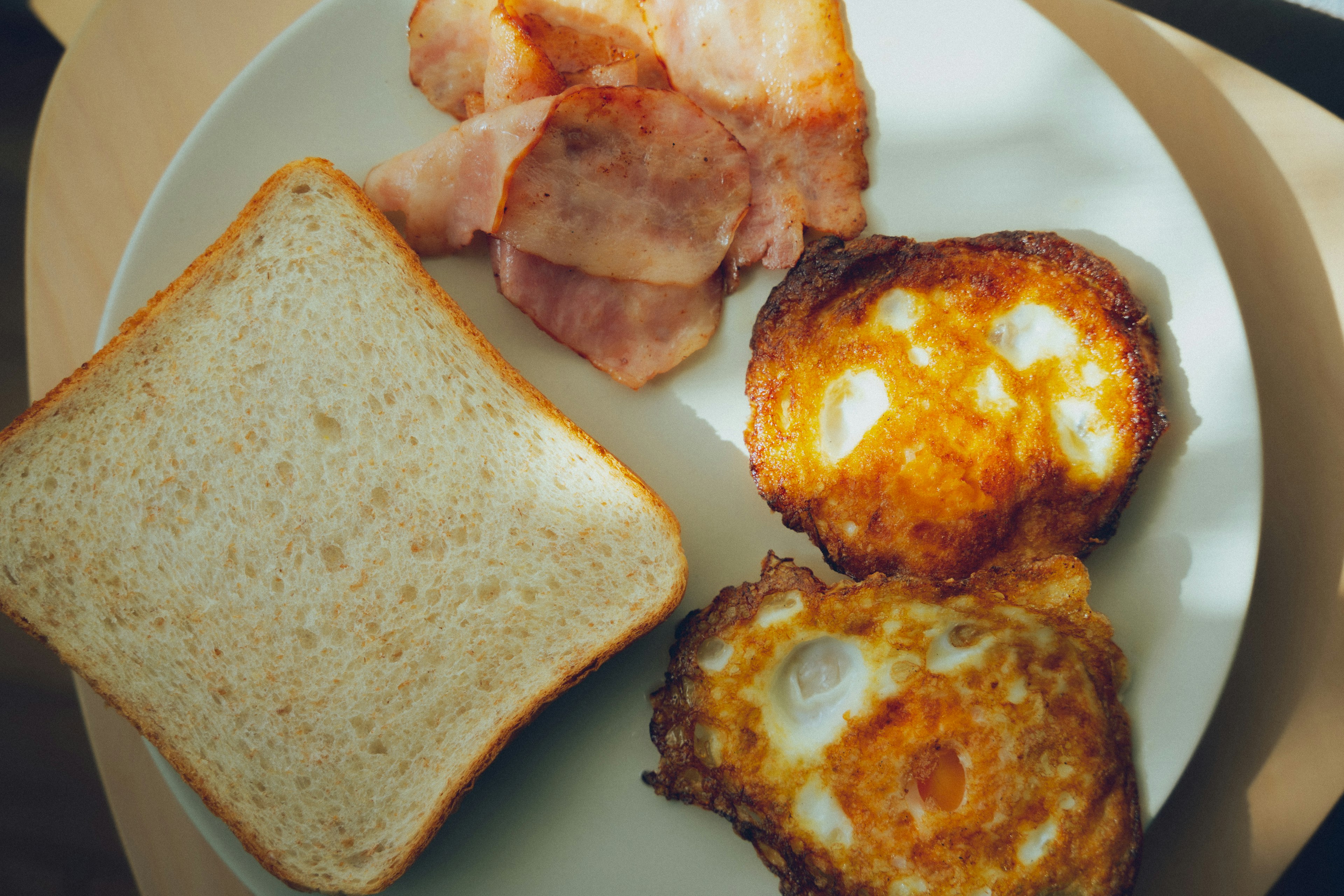 白い皿に盛られた朝食のプレートに、トースト、ベーコン、目玉焼きが盛り付けられている