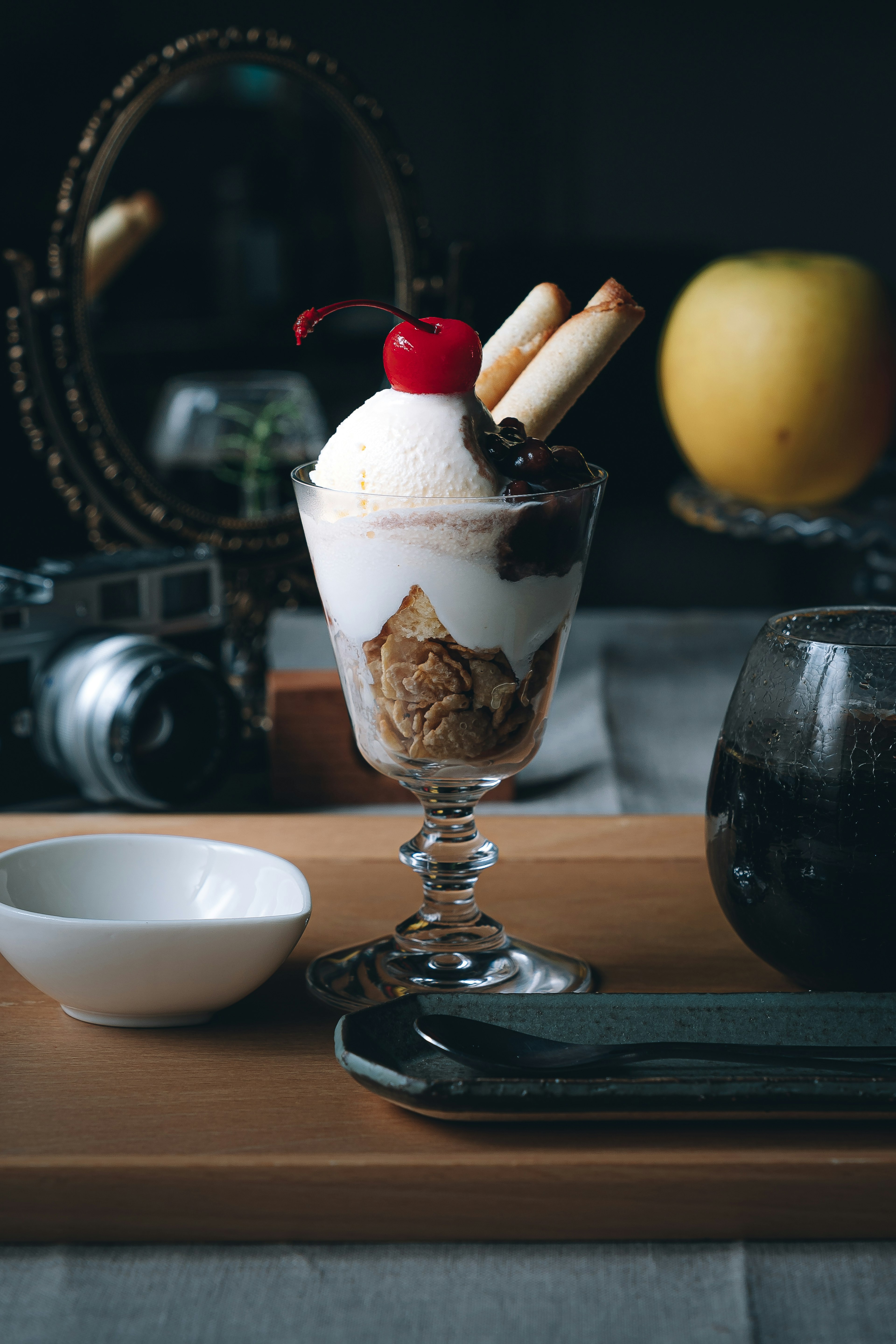 A beautifully arranged dessert parfait topped with cream and a cherry alongside a vintage camera