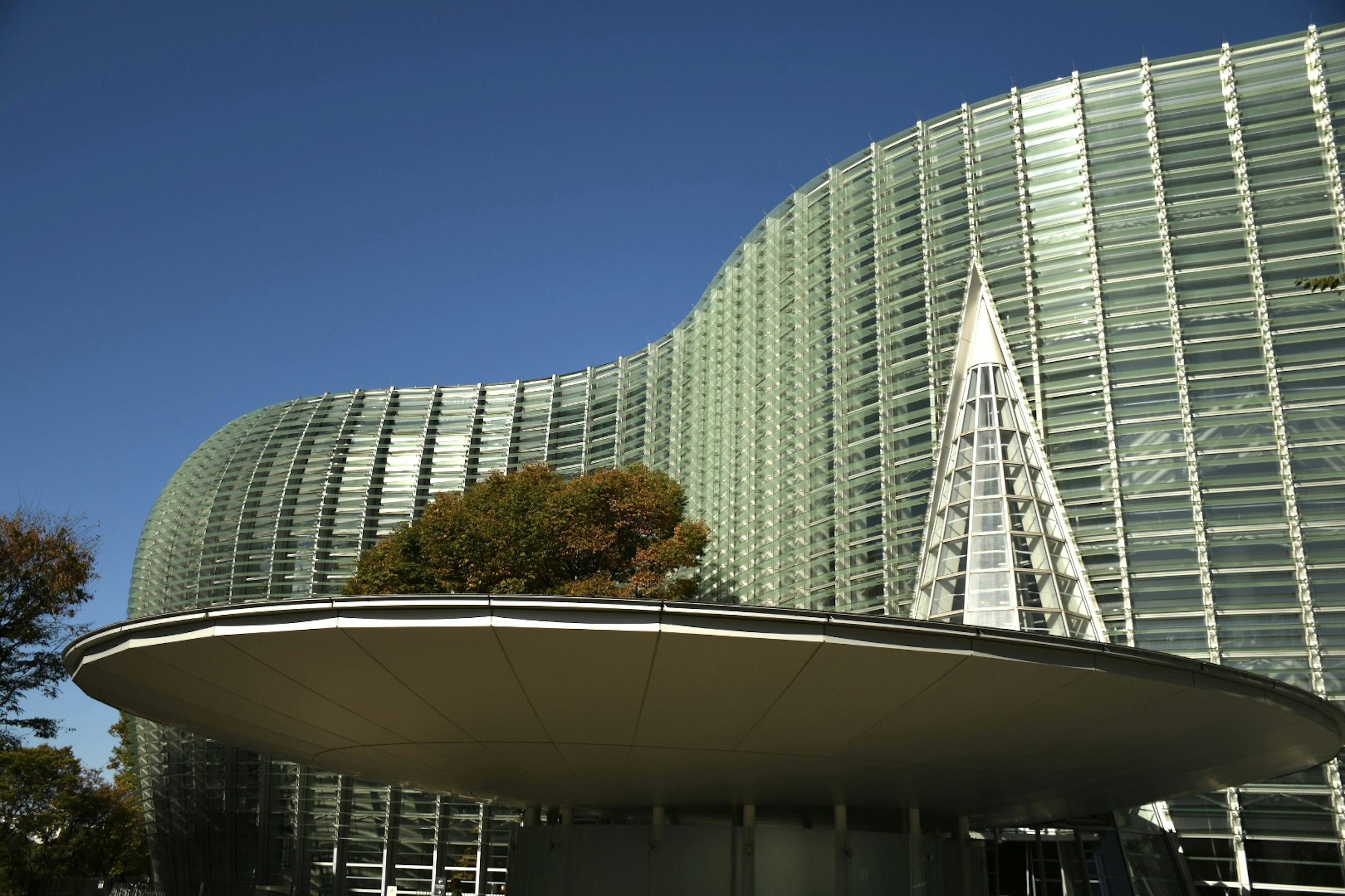 Exterior de un edificio moderno con fachada de vidrio ondulada y una aguja puntiaguda en la parte superior