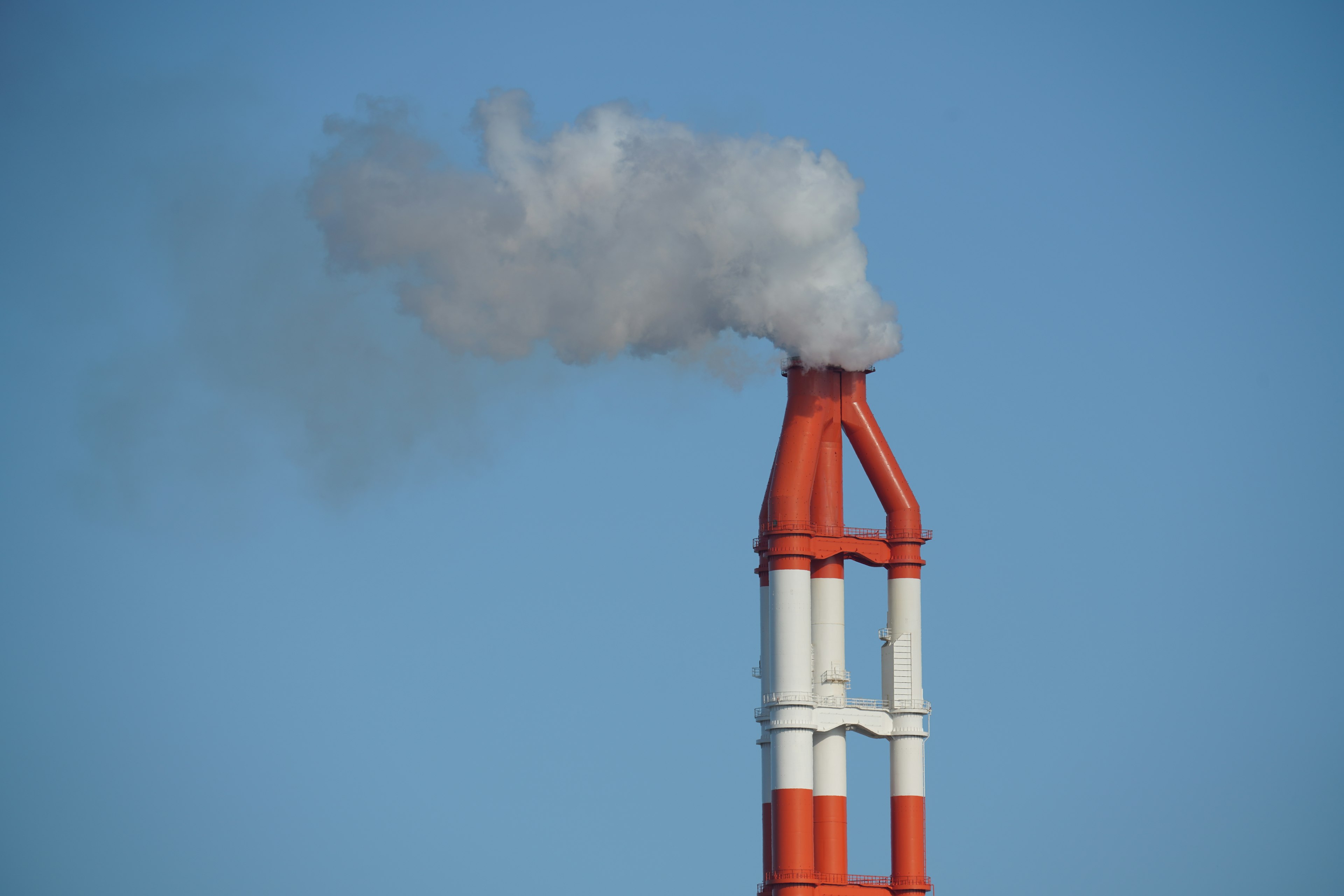 Red and white smokestack emitting smoke against a blue sky