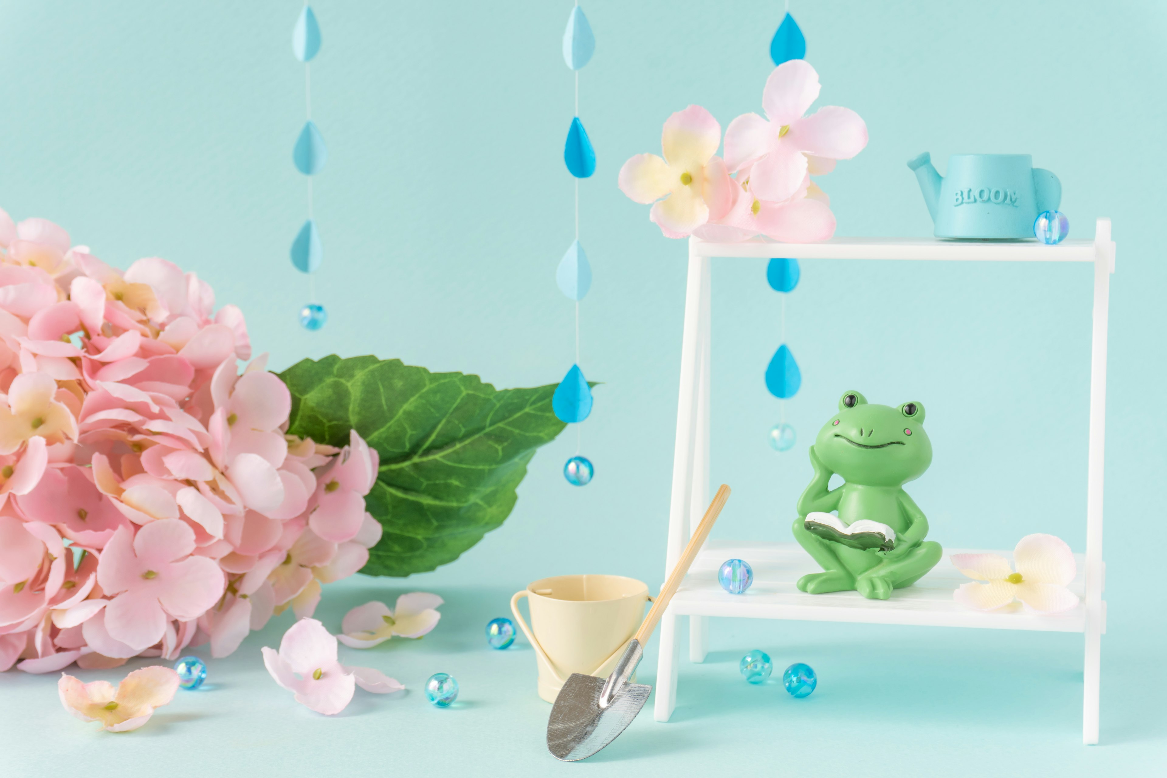 A green frog figurine surrounded by pink flowers against a blue background