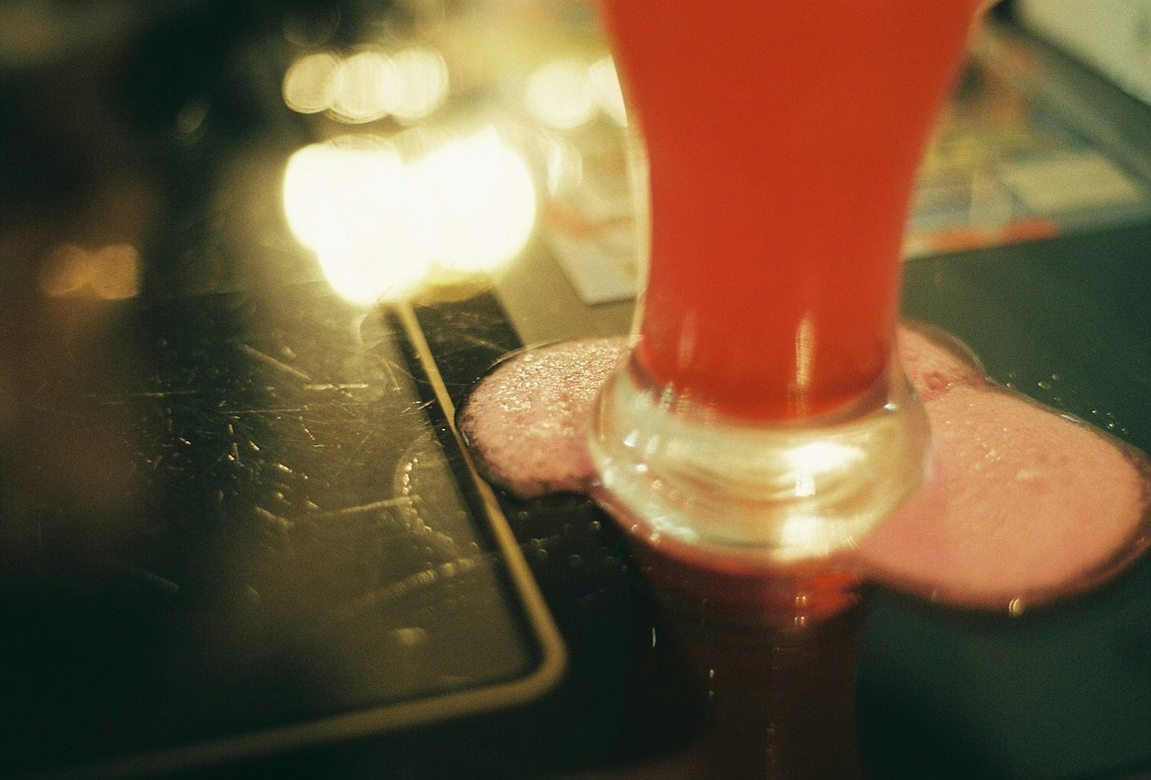 Un verre transparent avec une boisson rouge et de la mousse en dessous