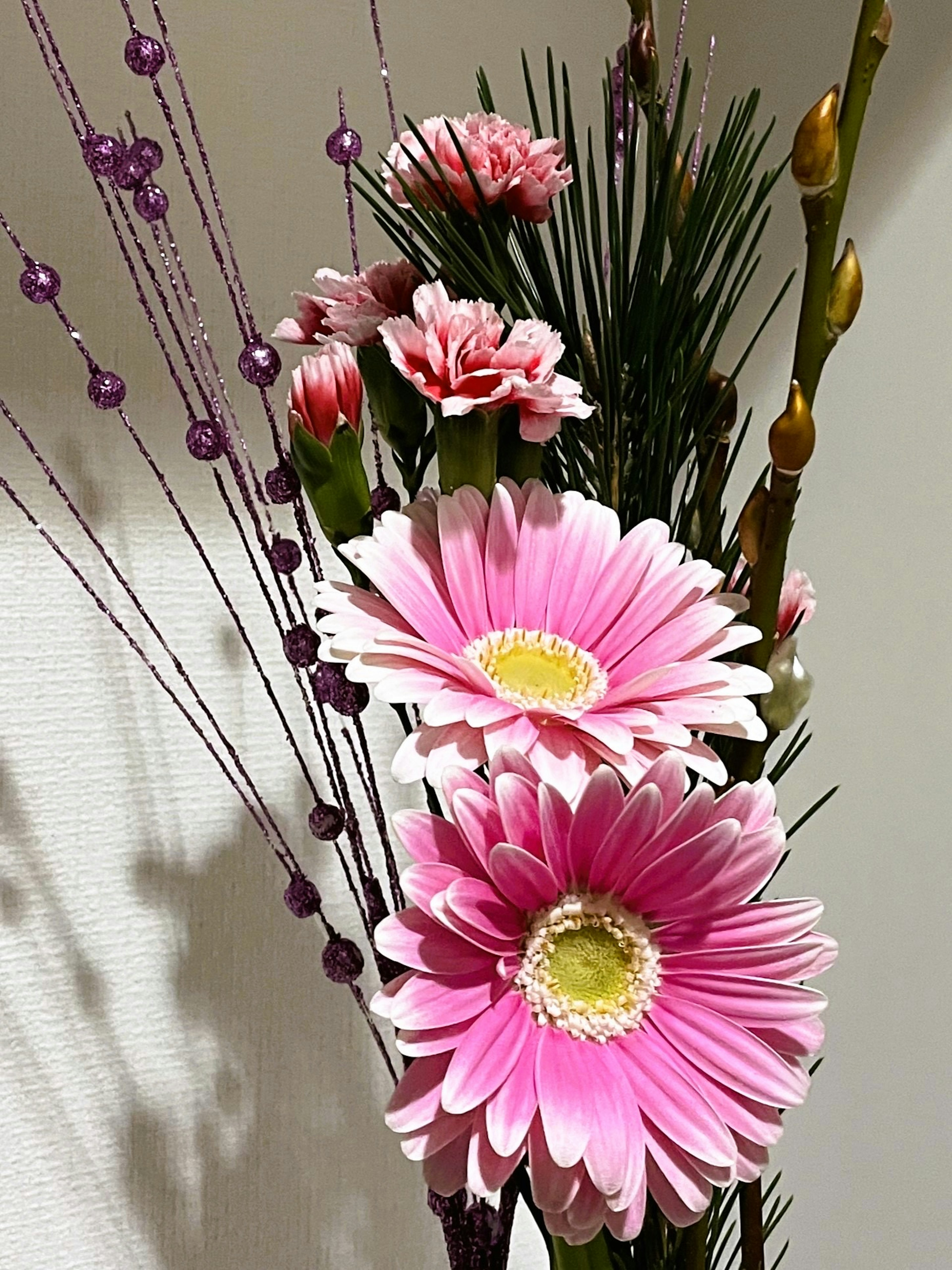 Floral arrangement featuring pink gerbera daisies and carnations with green leaves and purple beads