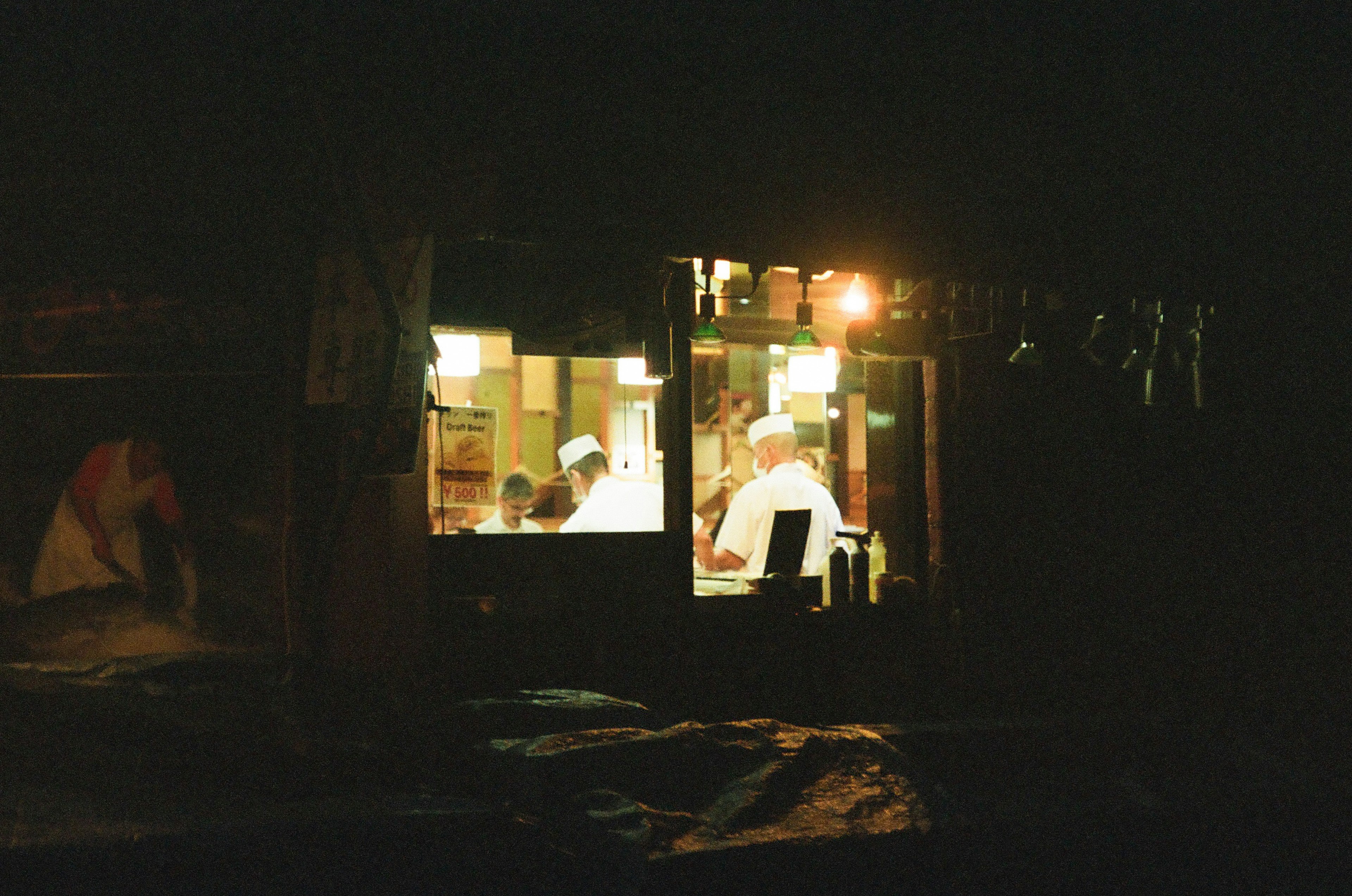 暗い夜に明かりがついた小さな店内で働く人々の姿